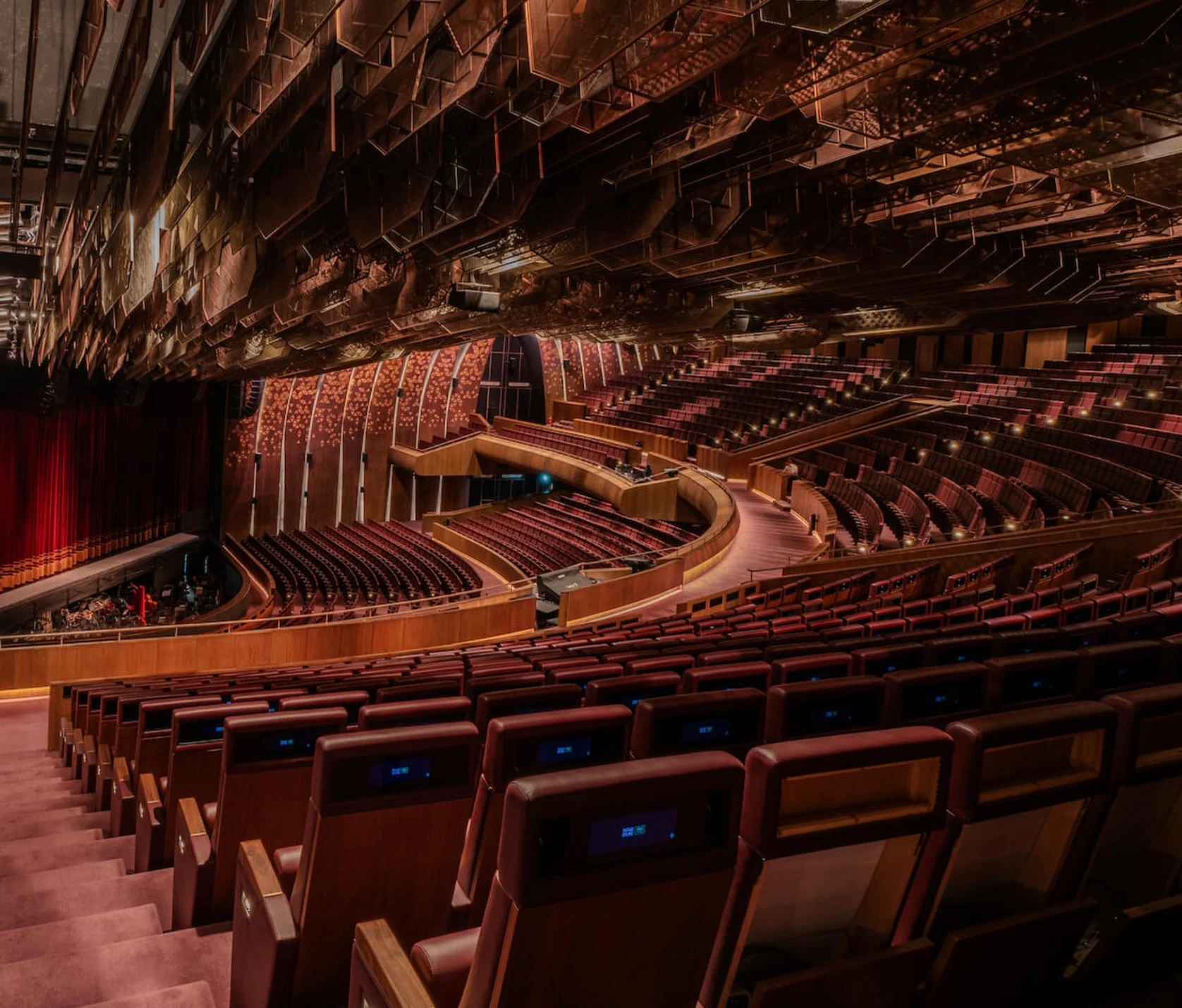 Theatre interior from the side aisle: tiered red seats and balconies under a faceted copper ceiling – King Fahad Chair for Poltrona Frau, Riyadh, Saudi Arabia, 2024 – product design