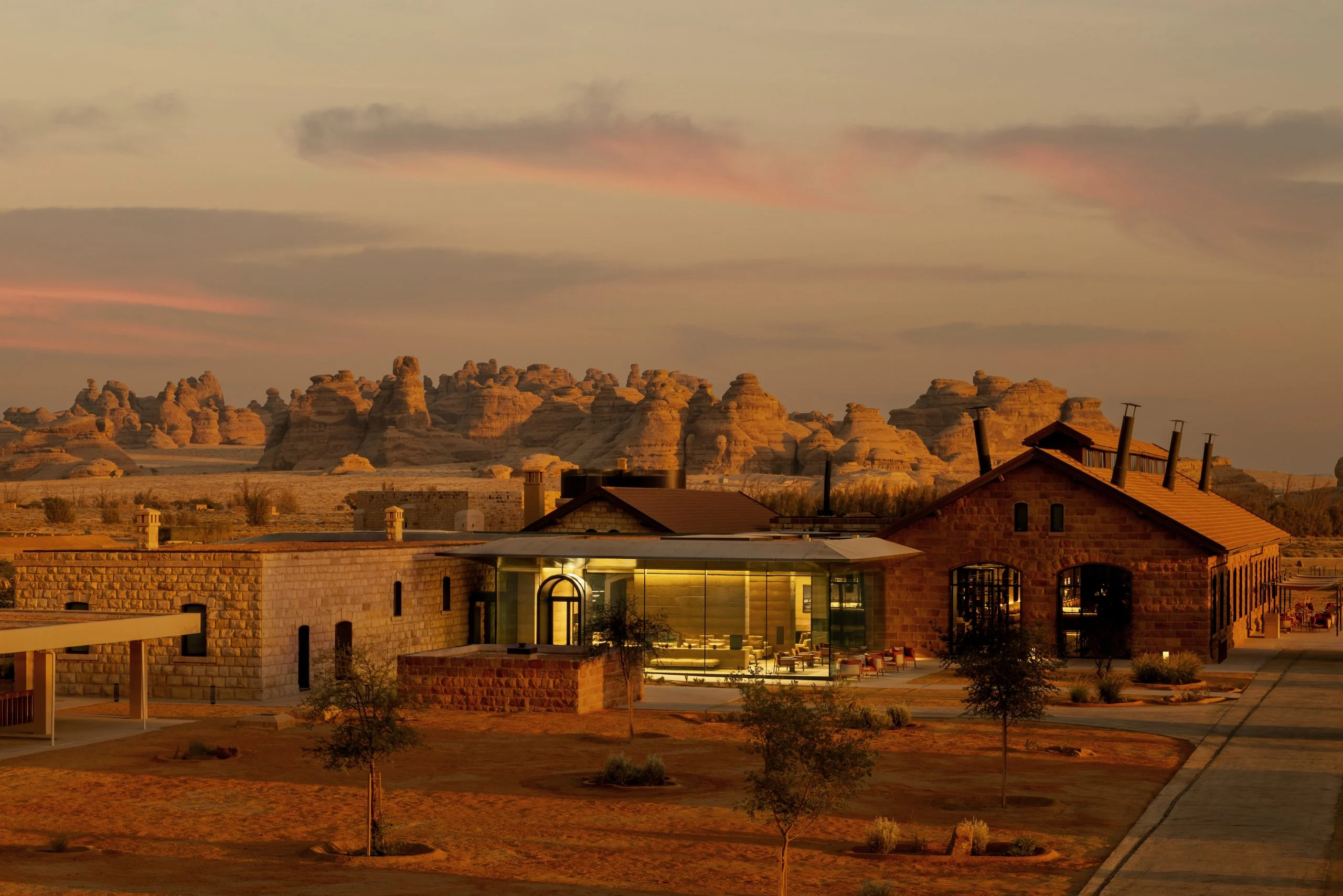 The Chedi Hegra at sunset: restored stone buildings and a glass pavilion against AlUla's rock formations – The Chedi Hegra, AlUla, Saudi Arabia, 2024 – hotel architecture