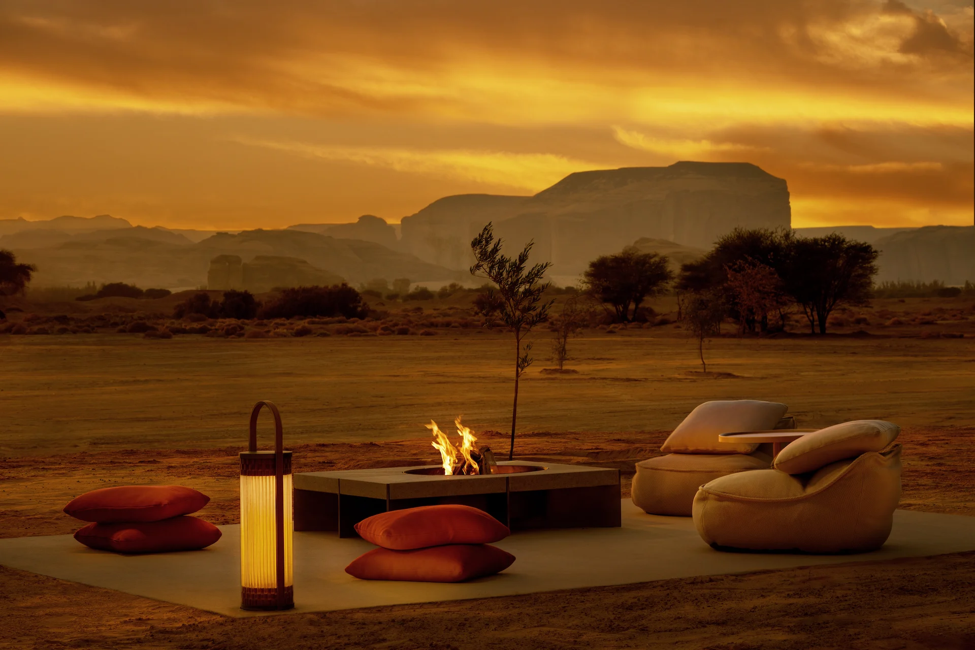Outdoor fire pit with floor cushions, lantern and lounge chairs in the desert under an orange sunset sky – The Chedi Hegra, AlUla, Saudi Arabia, 2024 – hotel architecture