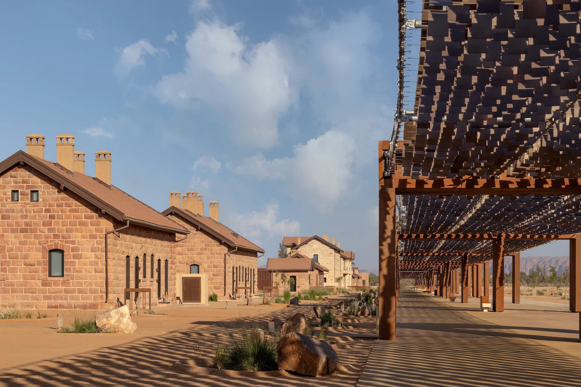 Row of restored stone station buildings beside a timber pergola casting striped shadows – The Chedi Hegra, AlUla, Saudi Arabia, 2024 – hotel architecture