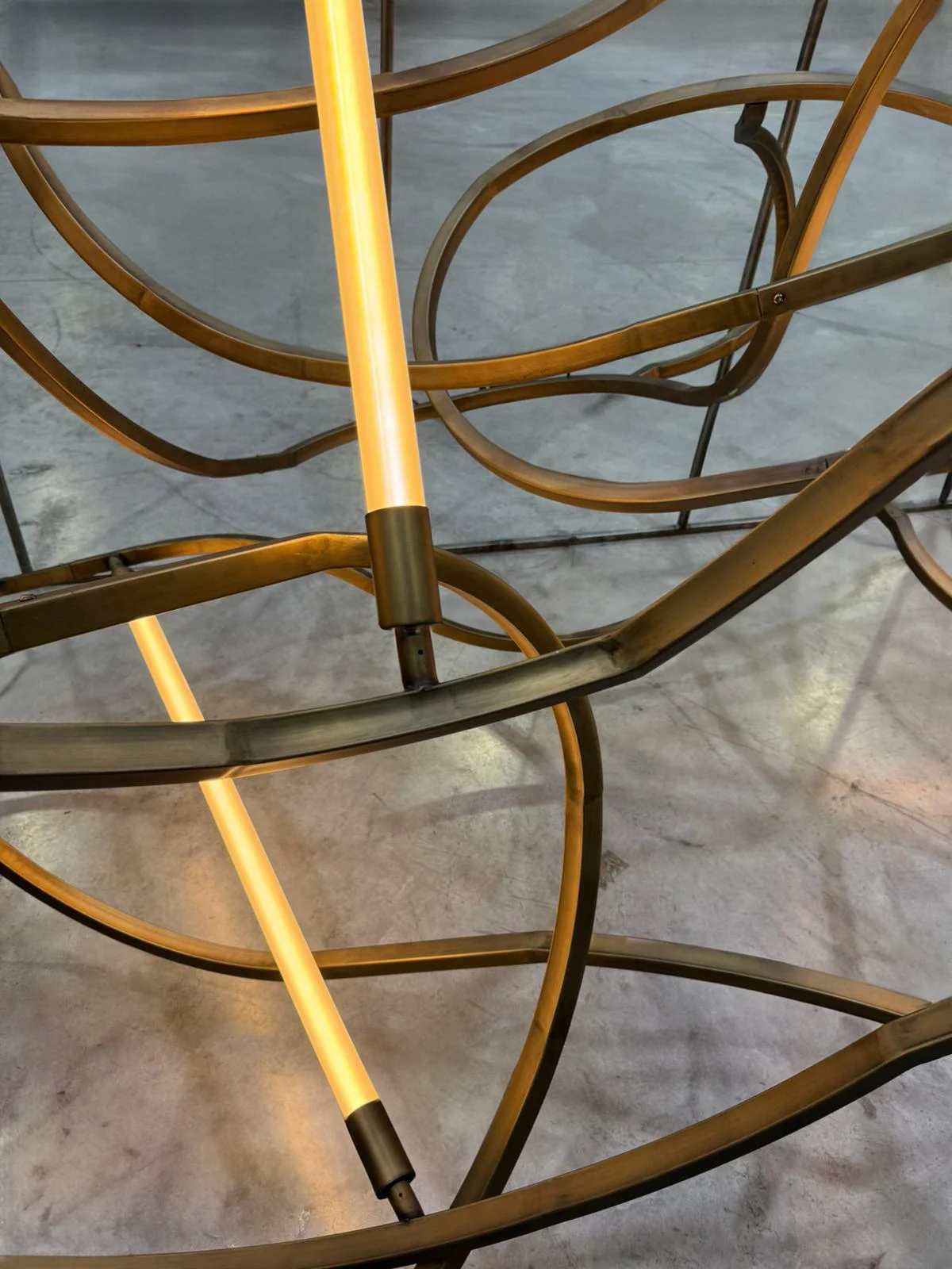 Detail of the curved rail sections and an illuminated light tube with brass fittings – The Chedi Hegra Chandelier, AlUla, Saudi Arabia, 2025 – lighting design