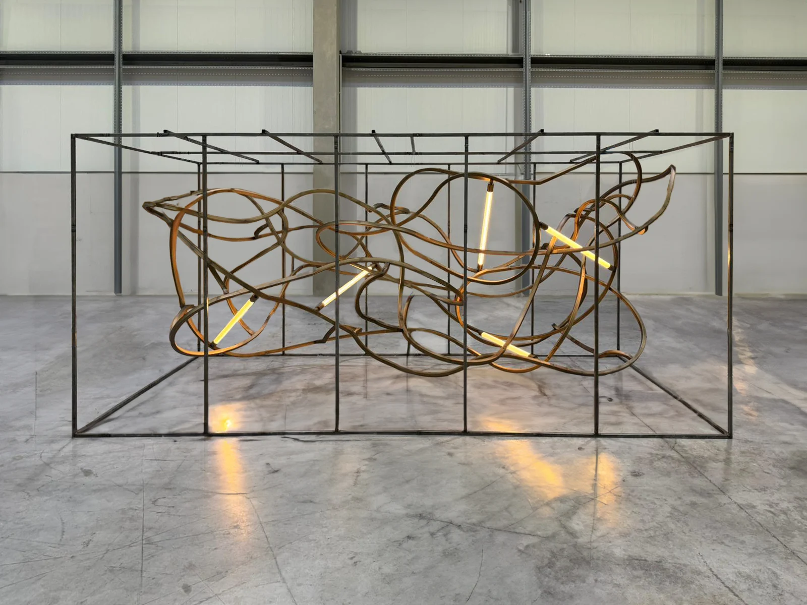Chandelier of bent old train rails tangled inside a steel frame, with glowing light tubes, in a workshop – The Chedi Hegra Chandelier, AlUla, Saudi Arabia, 2025 – lighting design