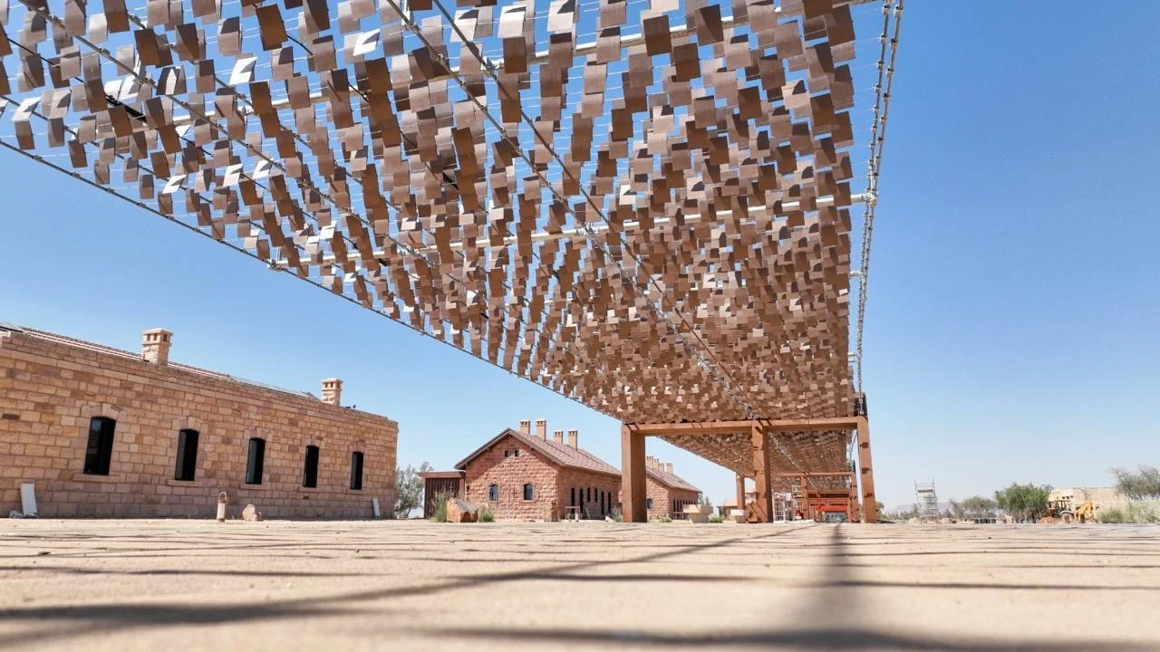 Low view up at the canopy's thousands of small metal pieces against blue sky, stone houses alongside – The Chedi Hegra Art Canopy, AlUla, Saudi Arabia, 2025 – architecture