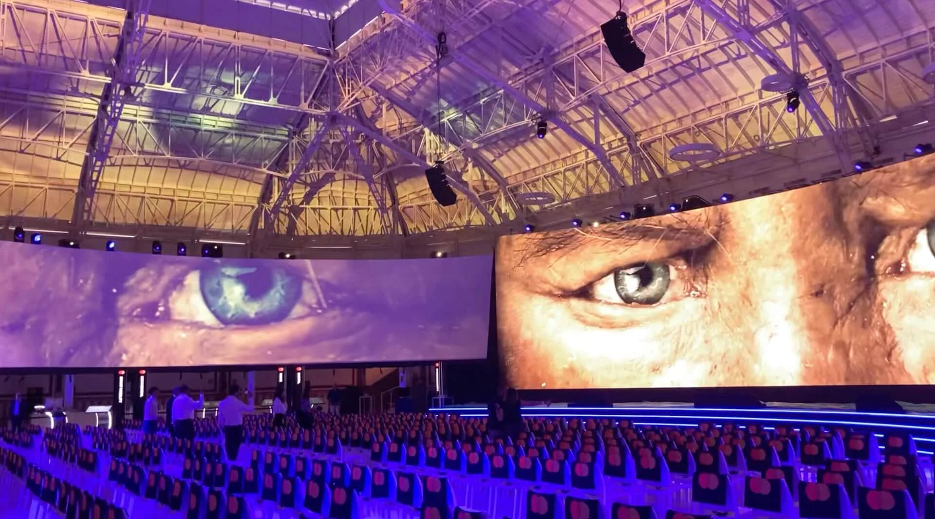 Mastercard Innovation Forum hall: curved LED screens showing giant eyes above rows of chairs, purple light – Mastercard Innovation Forum 2024, Milan, Italy – event design