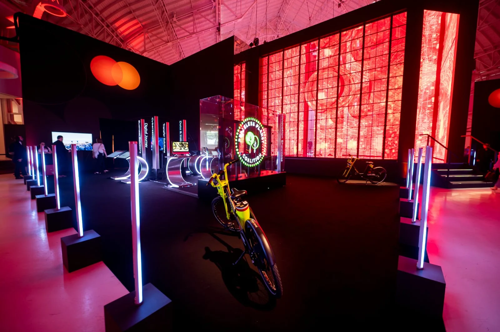 Mastercard Innovation Forum Demo Area: neon light posts, a yellow e-bike and a glass cube under red LED walls – Mastercard Innovation Forum 2023, Milan, Italy – event design