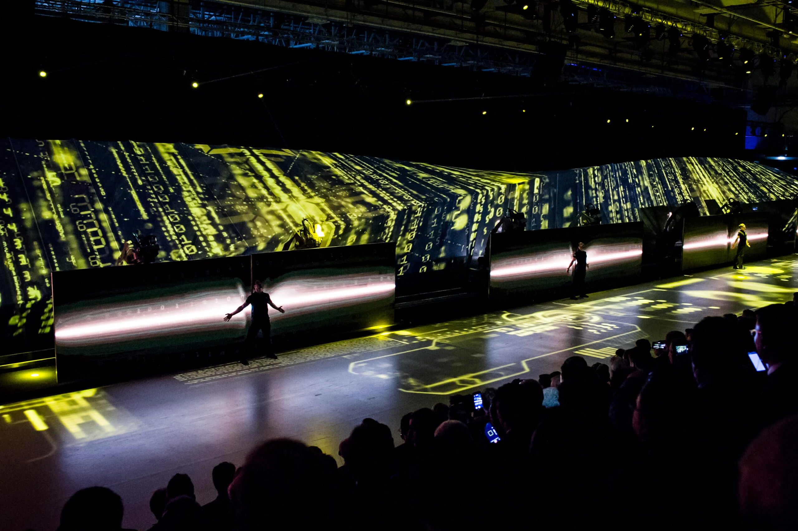 Performers on the long stage in front of screens with green data projections, audience filming with phones – Lamborghini Urus World Premiere, Sant'Agata Bolognese, Italy, 2017 – event design