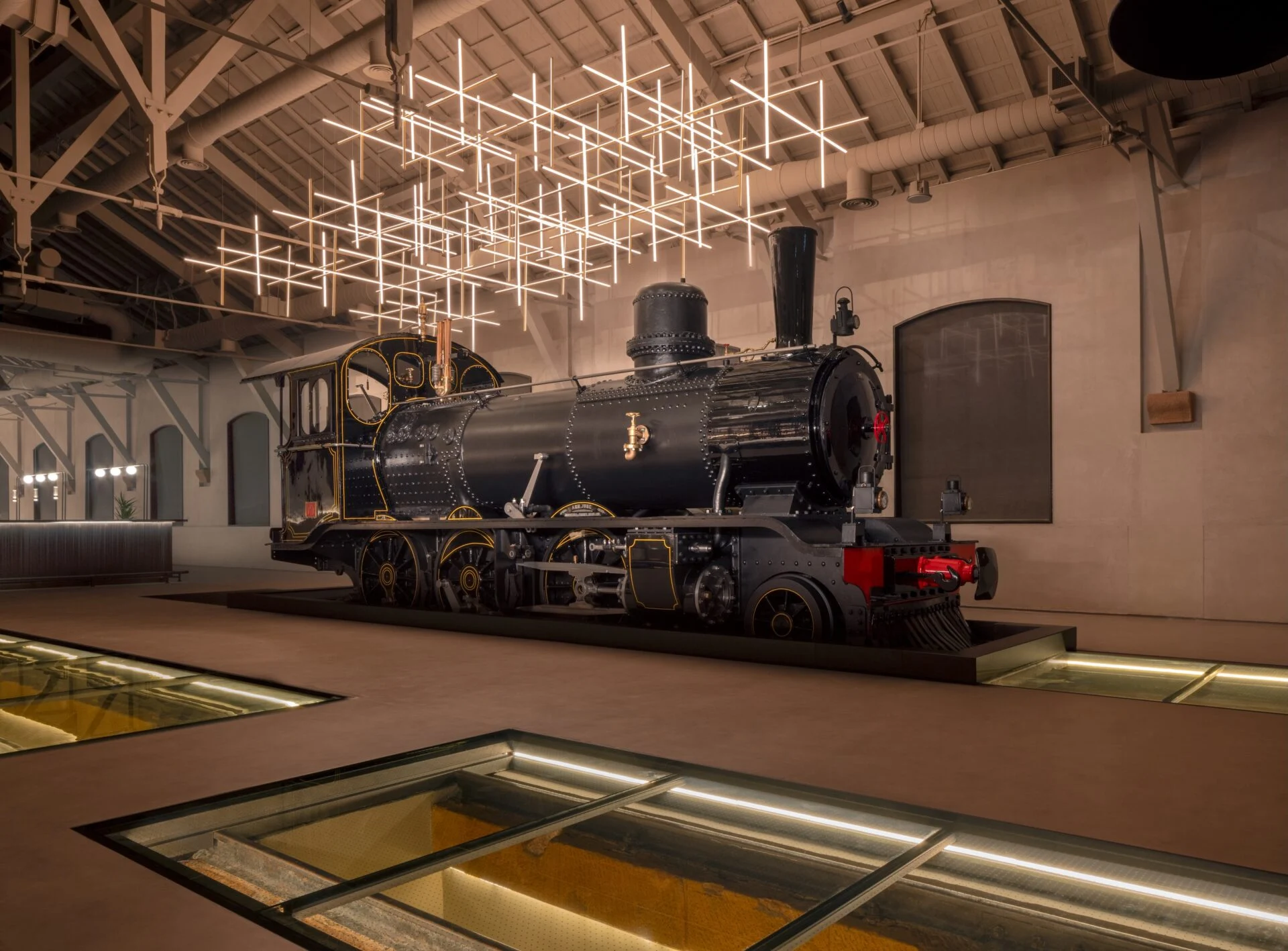 Historic black steam locomotive displayed indoors under a grid-like light installation and glass floor panels – The Chedi Hegra, AlUla, Saudi Arabia, 2024 – hotel architecture