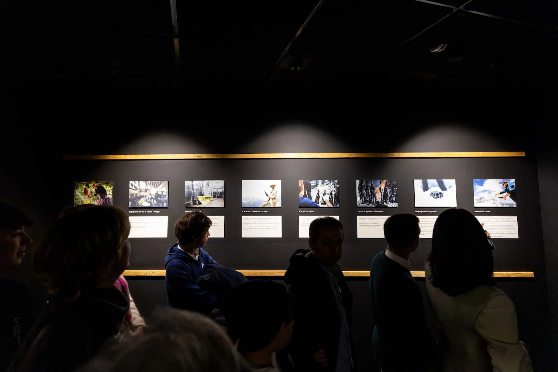 Visitors in front of a row of backlit photographs with captions on a dark wall – Cave Mont Blanc Winery at Skyway, Courmayeur, Italy, 2025 – interior and exhibition design