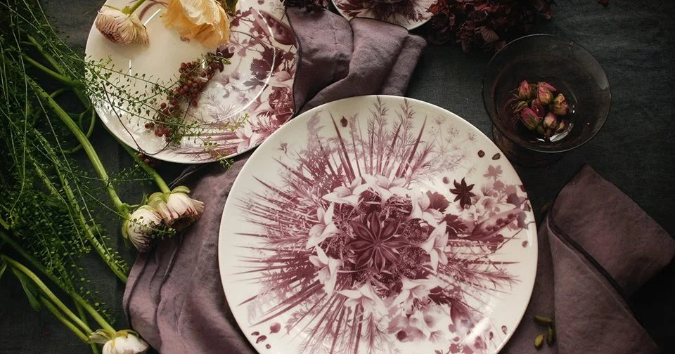 Top view of a plate with plum-coloured botanical decoration on grey linen, with flowers and a glass – Botanica Tableware for Bitossi Home, 2017 – product design