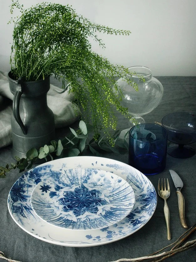 Blue botanical plates stacked on a grey tablecloth with cutlery, blue glasses and a jug of greenery – Botanica Tableware for Bitossi Home, 2017 – product design