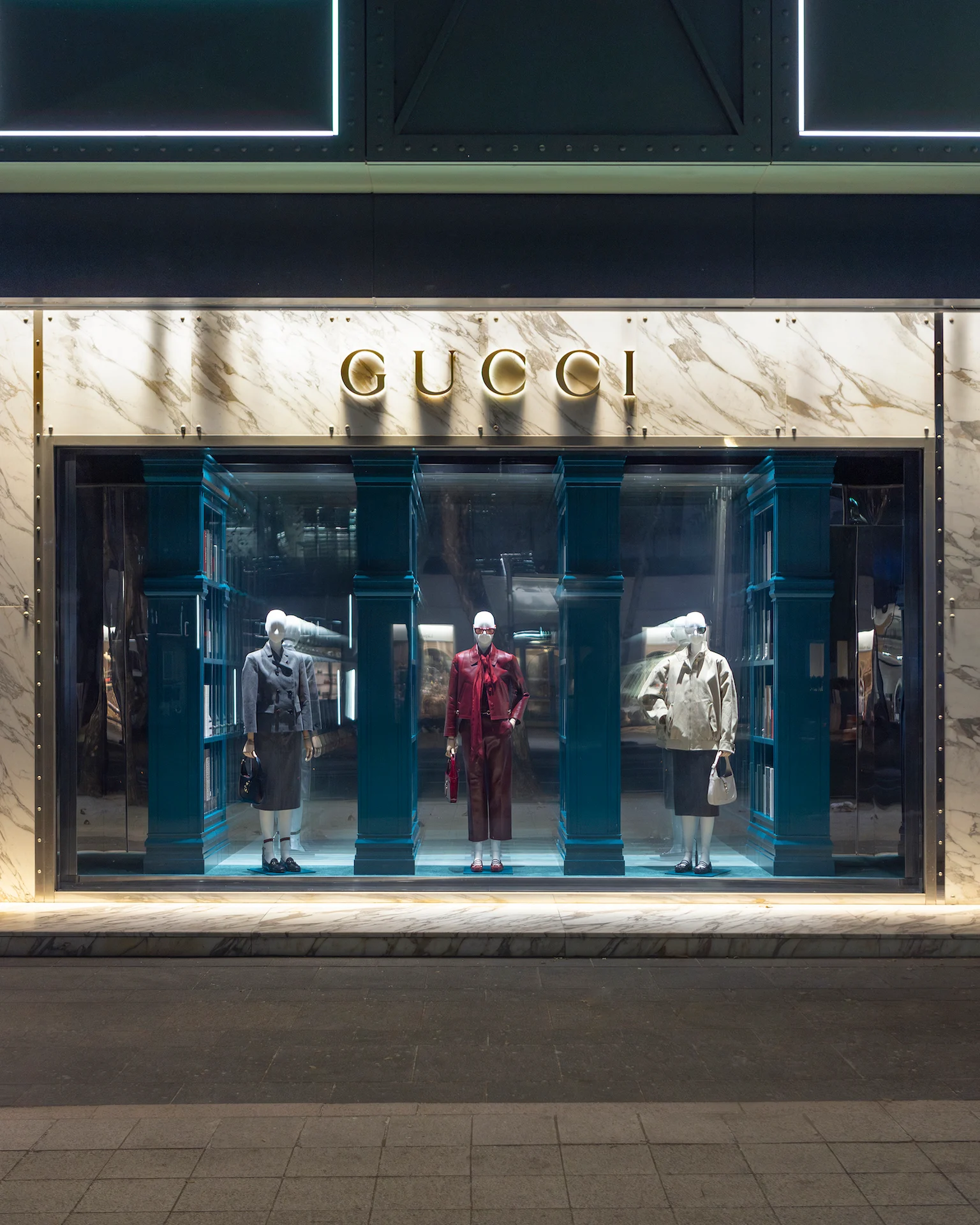 Gucci window in a marble façade: three mannequins between blue-green columns and mirrored bookcases – Gucci Endless Narratives Window Displays, 2025 – retail design