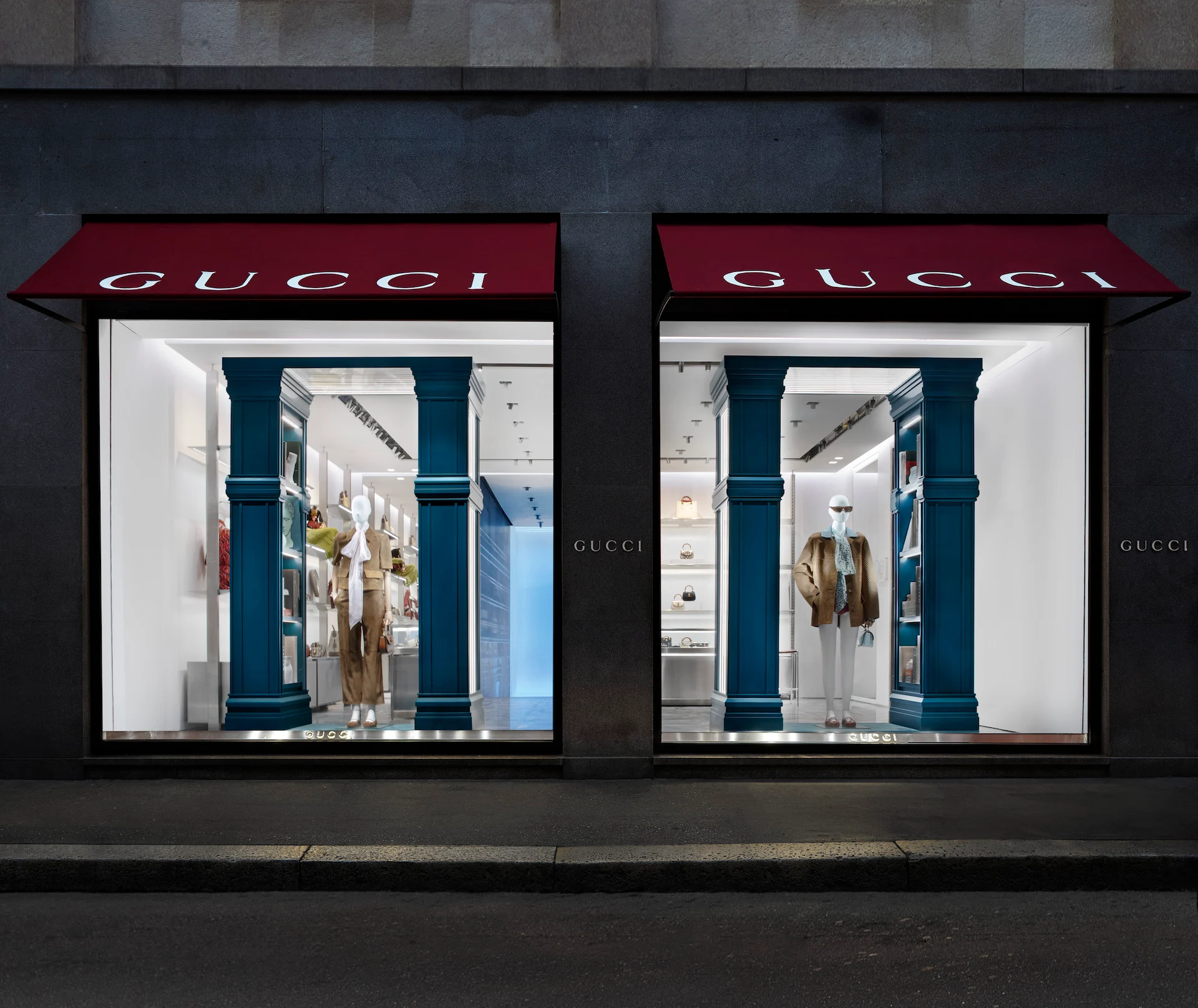 Two Gucci windows at night under red awnings, framed by blue-green columns with mannequins and lit shelves – Gucci Endless Narratives Window Displays, 2025 – retail design
