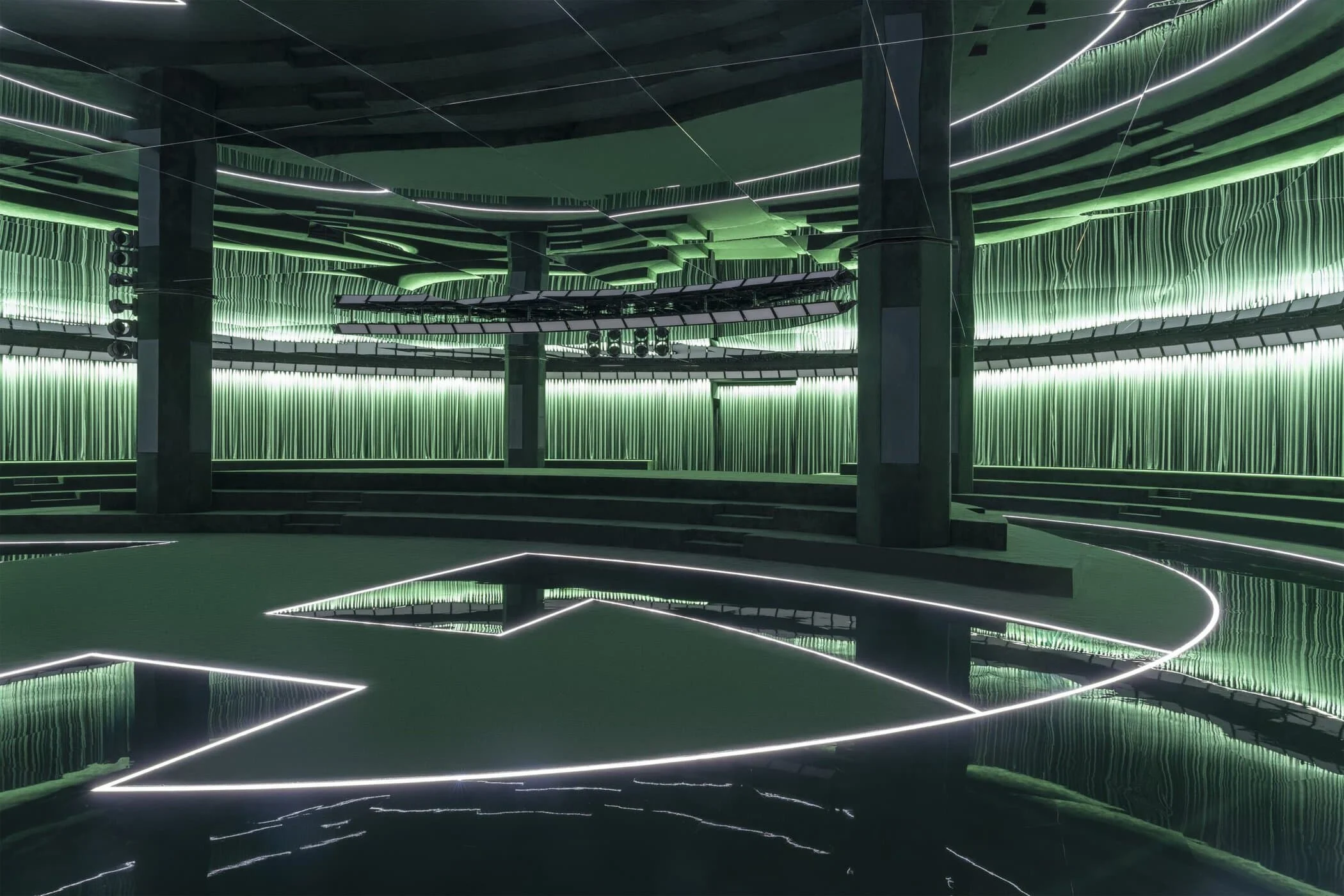Wide view of the empty show venue with the Interlocking G drawn in light on the mirrored floor – Gucci Fall/Winter 2025, Milan, Italy – fashion show set design