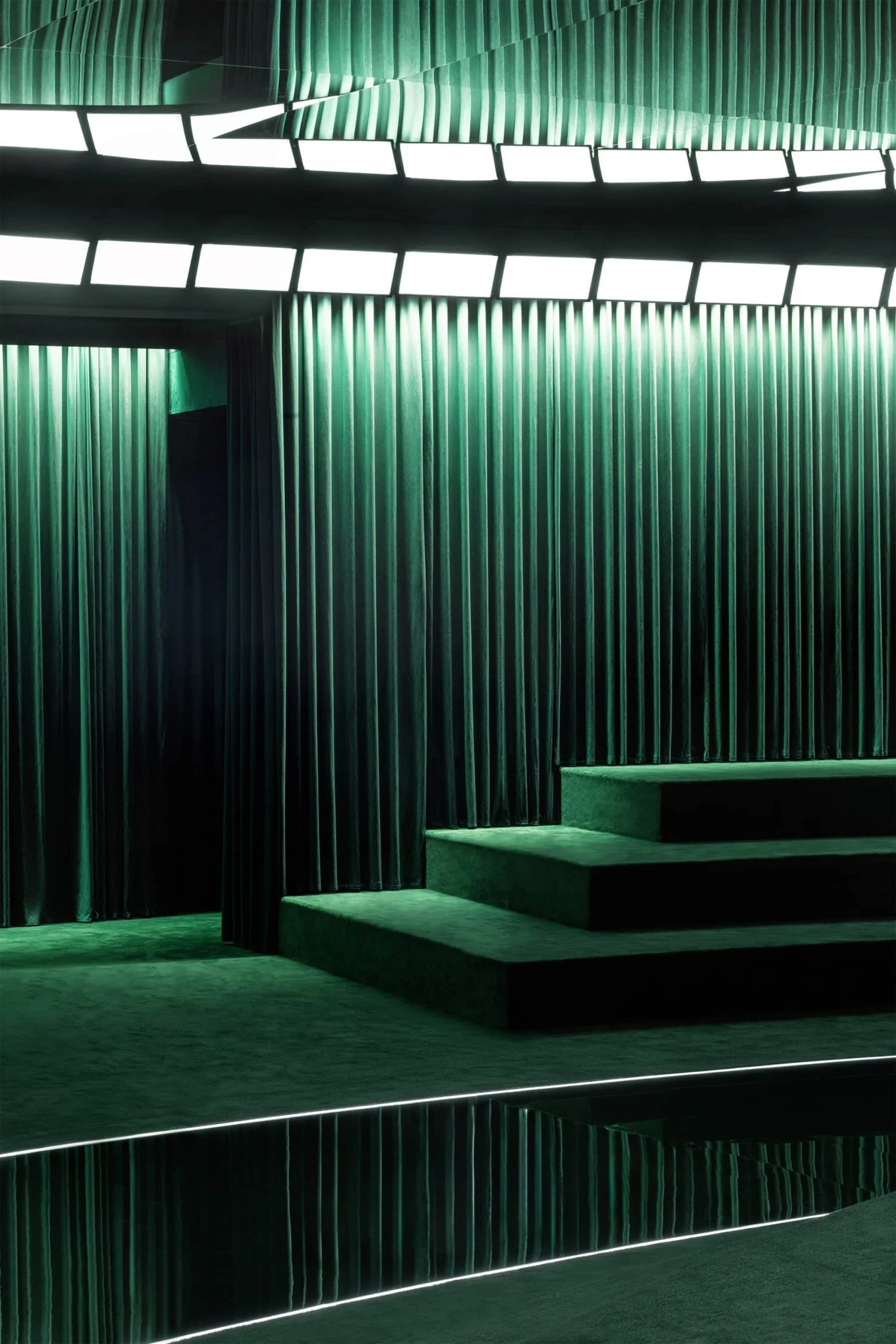 Detail of green velvet steps and pleated curtains lit by a ring of white light panels – Gucci Fall/Winter 2025, Milan, Italy – fashion show set design