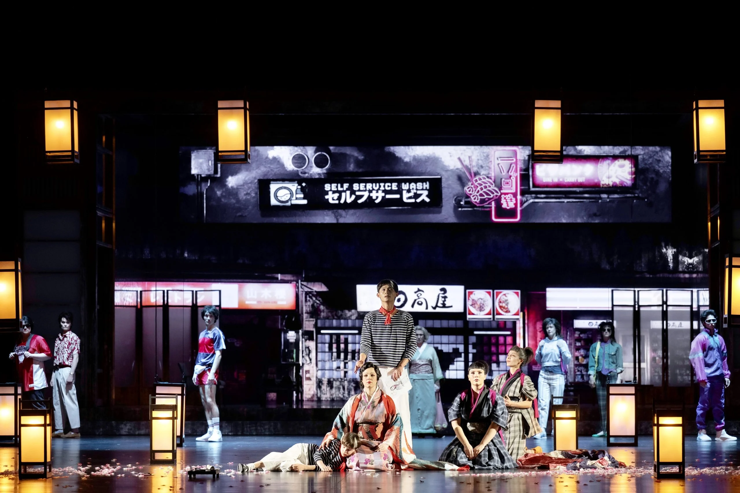 Chorus and soloists on the modern Japanese street set, lit by paper lanterns along the stage edge – Madama Butterfly at Festspielhaus Baden-Baden, Germany, 2025 – opera set design