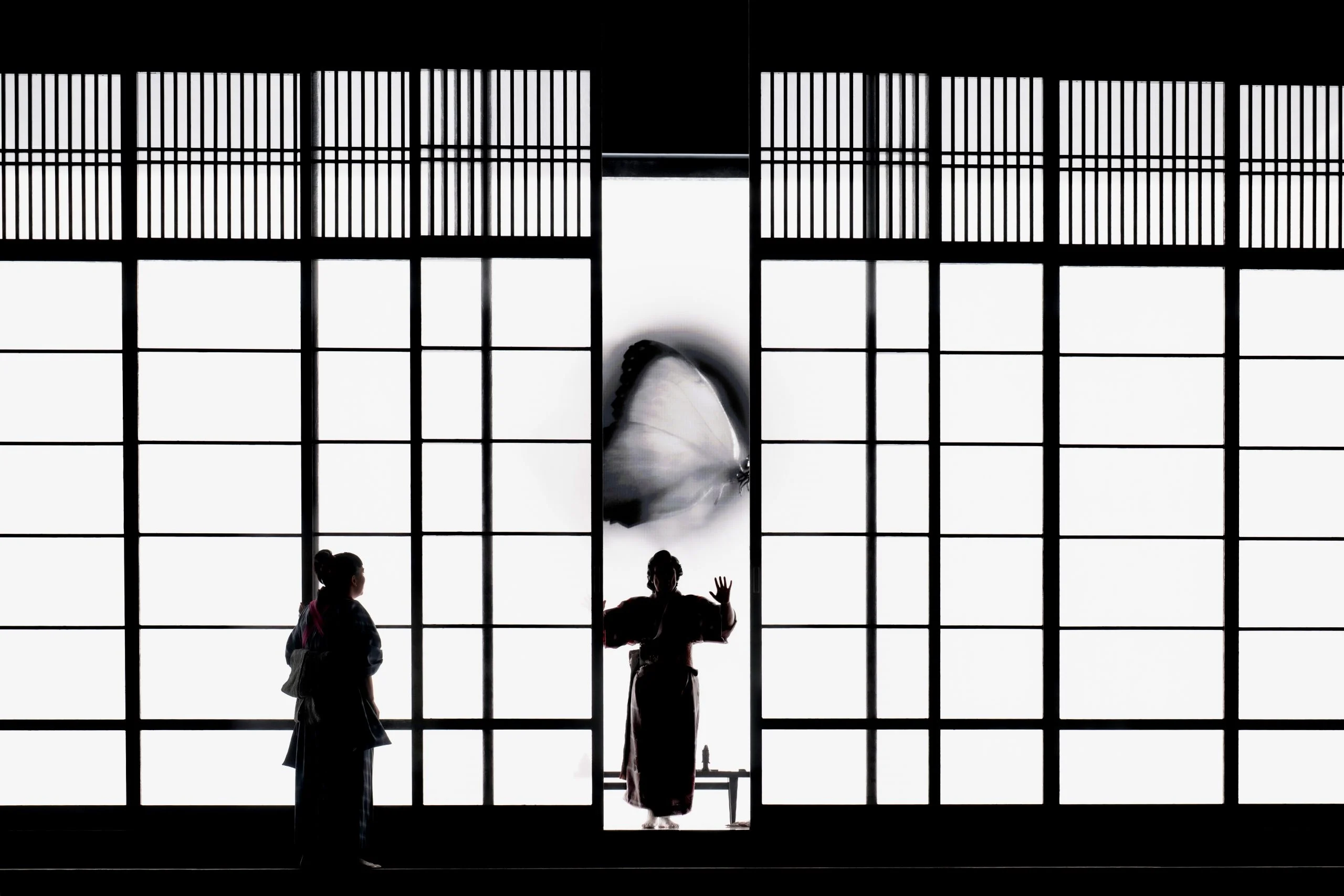 Silhouettes of two women before backlit shoji screens, a giant butterfly projected on the central panel – Madama Butterfly at Festspielhaus Baden-Baden, Germany, 2025 – opera set design