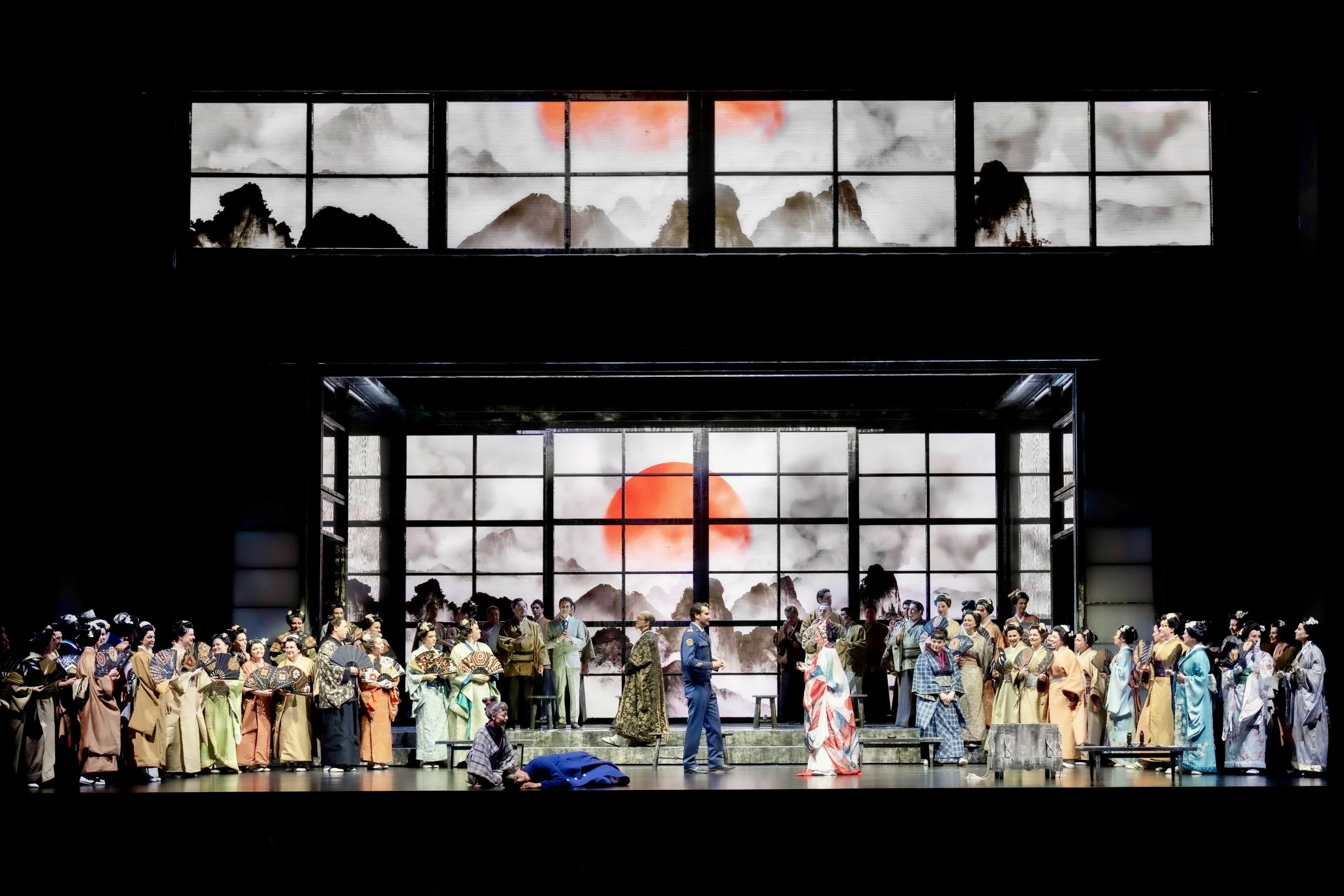 Full chorus in kimonos across the stage before glass screens showing a red sun over ink mountains – Madama Butterfly at Festspielhaus Baden-Baden, Germany, 2025 – opera set design