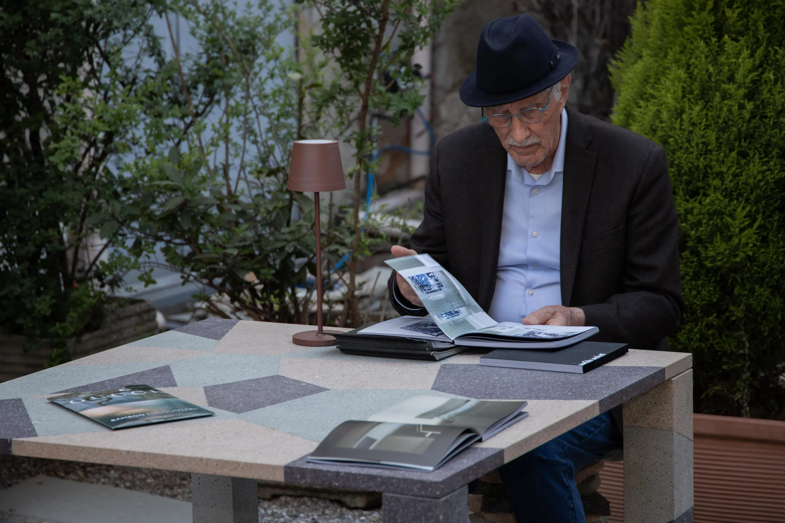 Guest reading a catalogue at an outdoor porphyry table with a geometric inlaid top – Everything Is a Party at Fuorisalone, Milan, Italy, 2025 – event design