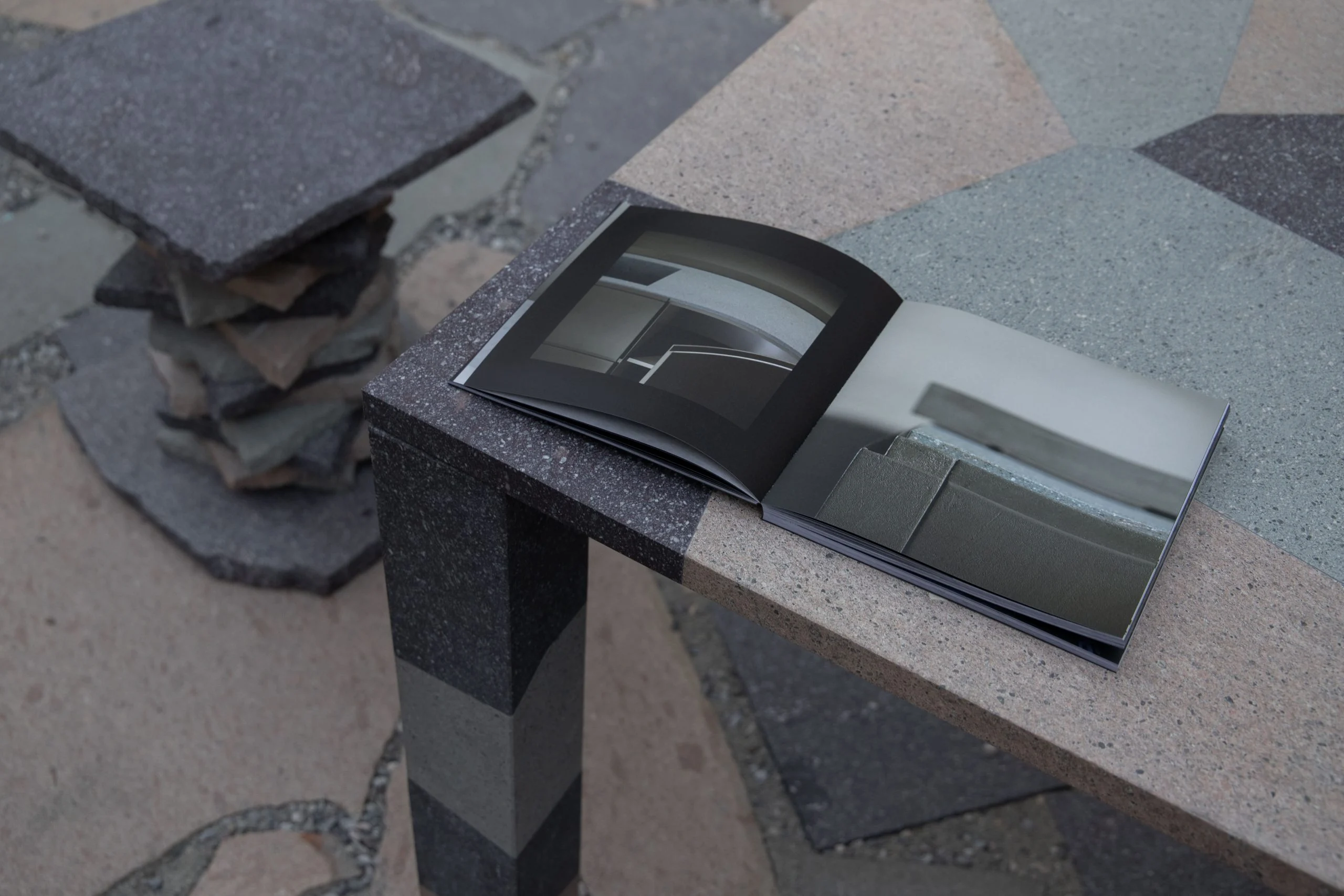 Book open on a porphyry table with geometric inlaid top, a stacked-stone stool behind – Everything Is a Party at Fuorisalone, Milan, Italy, 2025 – event design