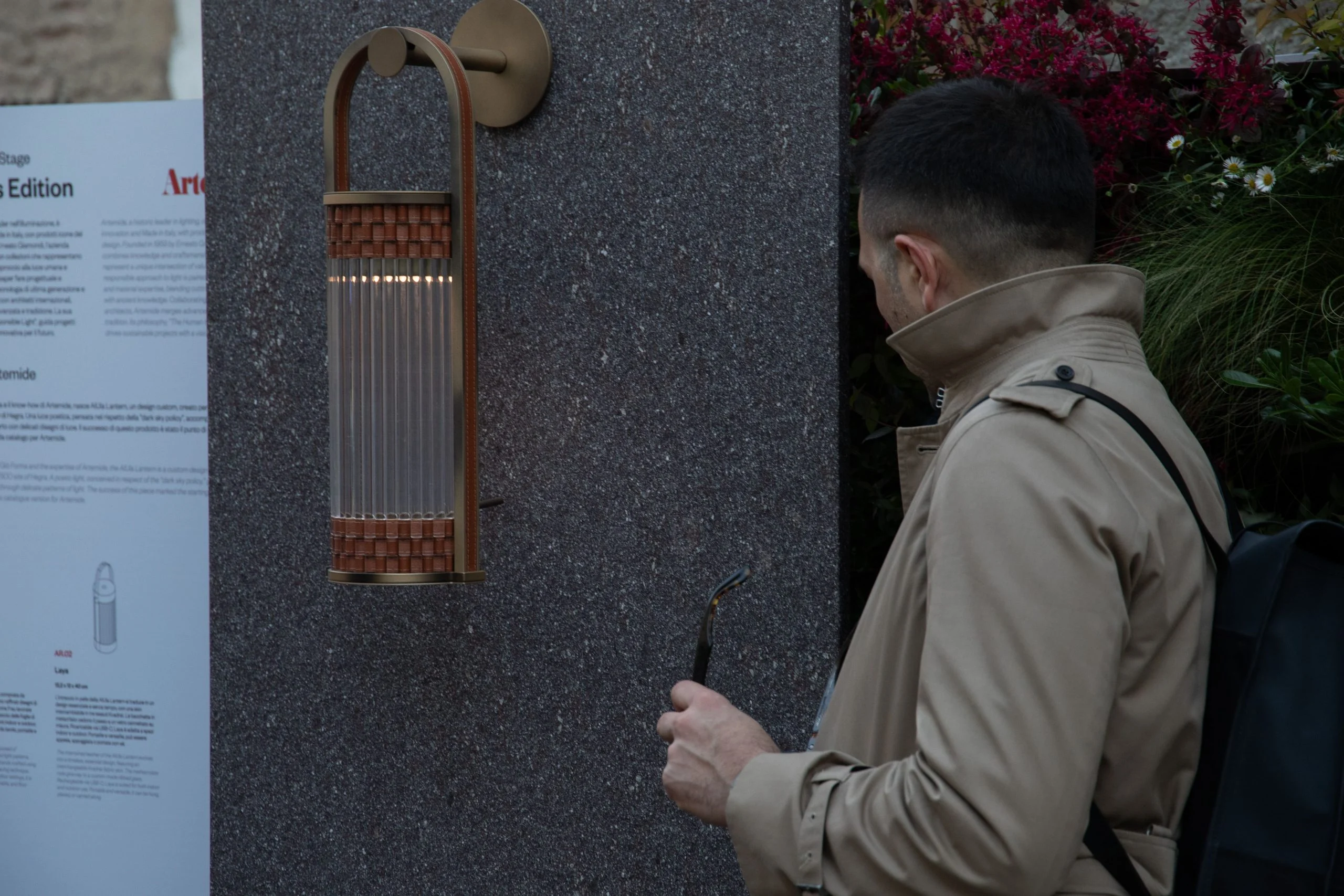 Guest looking at a bronze and glass wall lamp mounted on a dark stone panel – Everything Is a Party at Fuorisalone, Milan, Italy, 2025 – event design
