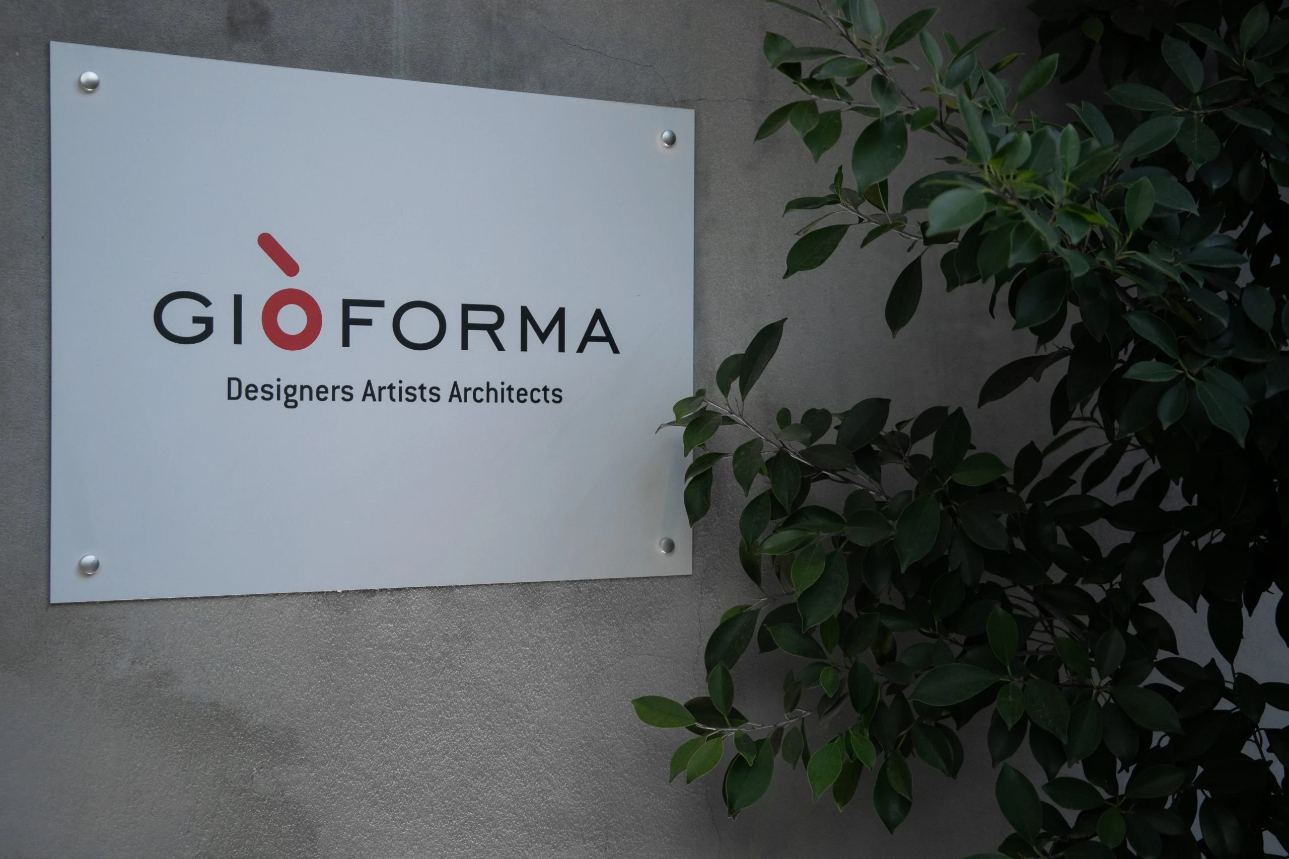 Studio sign with logo and the words Designers Artists Architects on a concrete wall beside a plant – Everything Is a Party at Fuorisalone, Milan, Italy, 2025 – event design