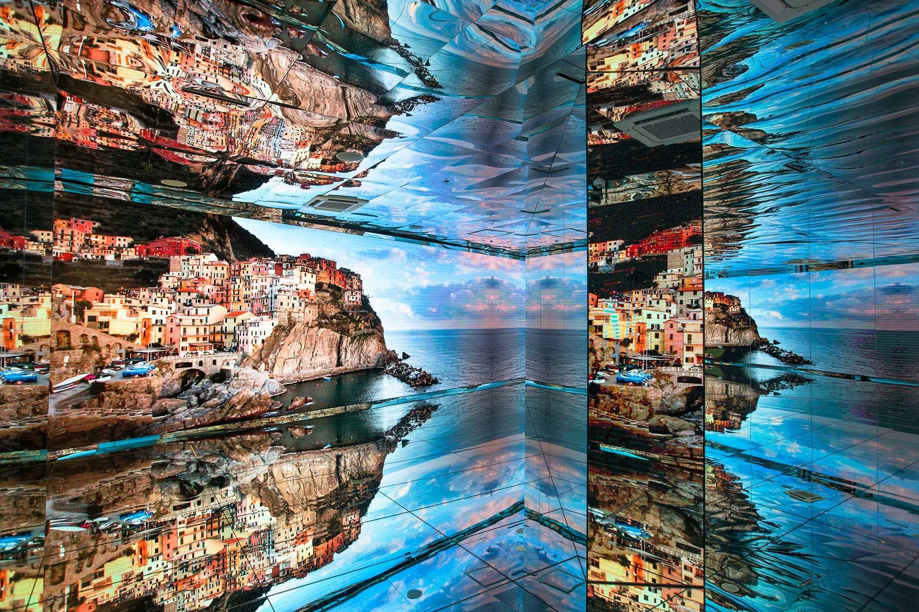 Mirrored room with screens showing a colourful cliffside seaside village, reflected on every surface – Italian Pavilion at Expo 2015, Milan, Italy – exhibition design