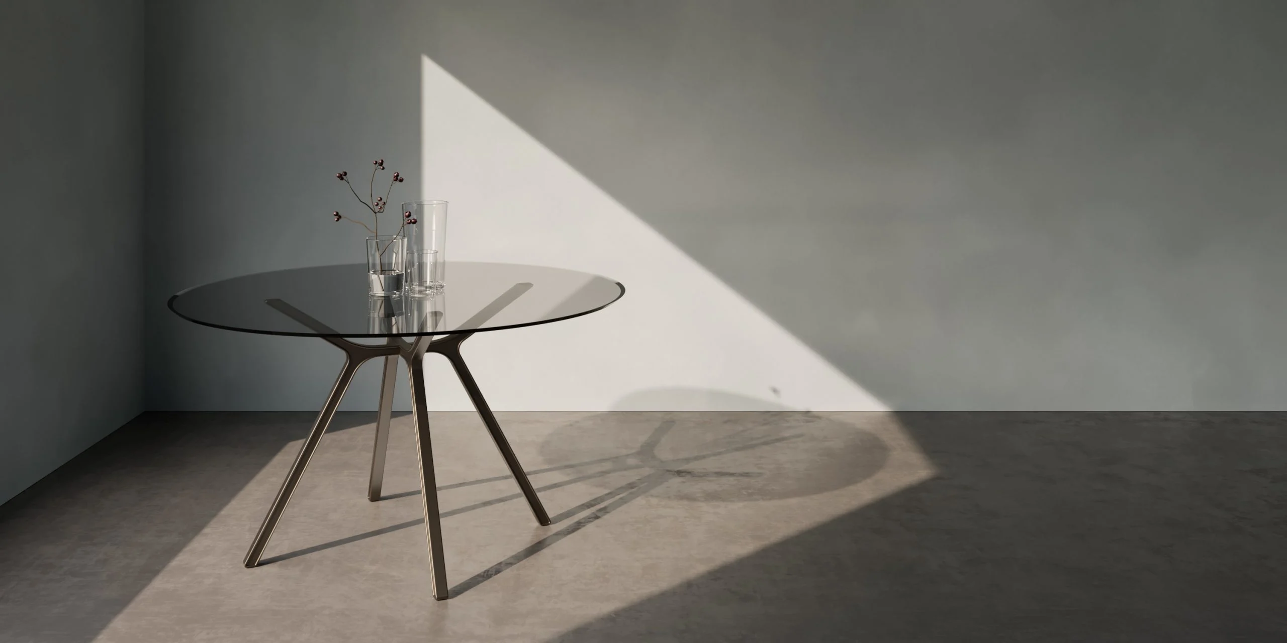 Round glass table with angled metal legs in a grey room crossed by a beam of sunlight – Tonino Lamborghini FRAME Collection, Milan, Italy, 2025 – product design