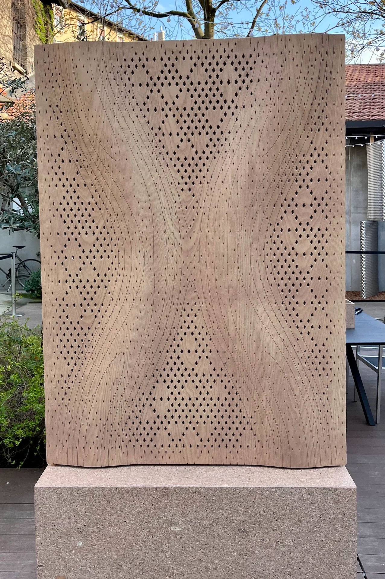 Wooden acoustic panel with a perforated diamond pattern and wavy surface on a stone base outdoors – Strong by Form Woodflow-Skin Panels, Milan, Italy, 2025 – product design