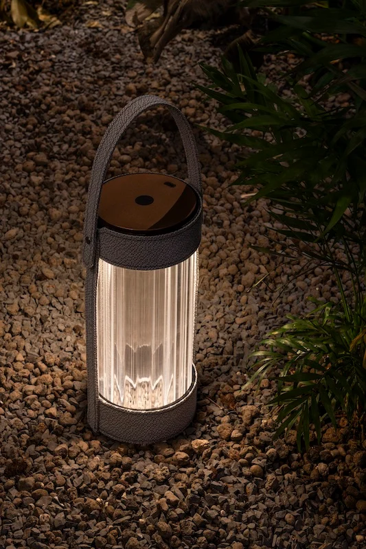 Lantern with a grey strap glowing on gravel among plants at night – AlUla Lantern for Artemide, Milan, Italy, 2025 – lighting design