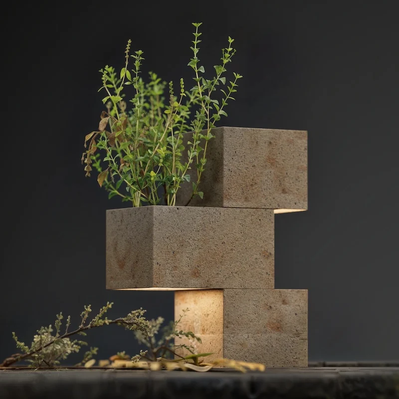 Lamp of three offset stone blocks with a plant growing from the top, light glowing from beneath – Porfido Pedretti Porphyry Furniture, Milan, Italy, 2025 – product design