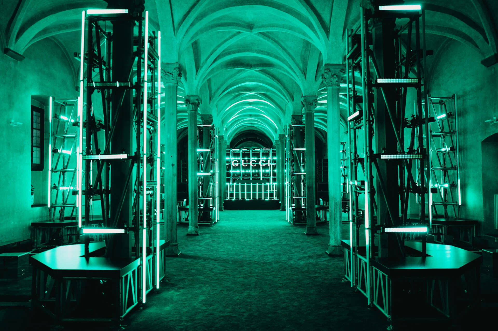 Vaulted hall bathed in green light, lit scaffolding towers leading to a GUCCI sign – Gucci Cruise 2026 Afterparty, Florence, Italy, 2025 – event design