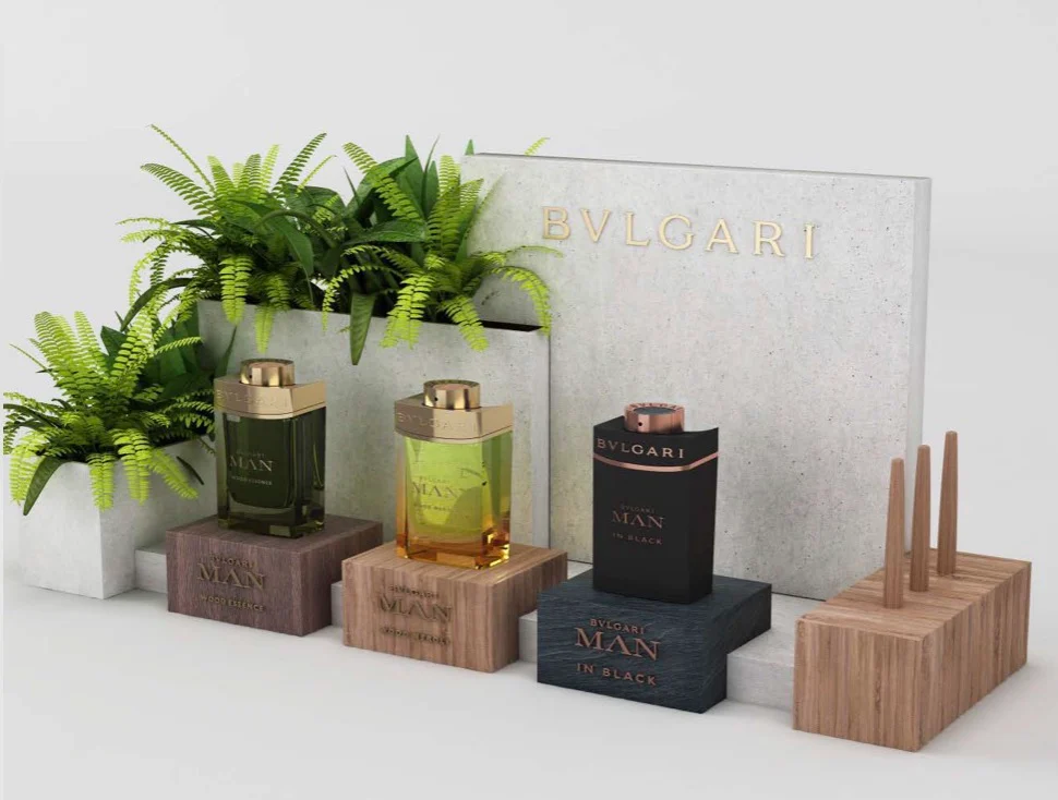 Render of a Bvlgari Man counter display: three fragrance bottles on wood blocks before a concrete panel and ferns – Bvlgari Man Wood Neroli, 2019 – retail design