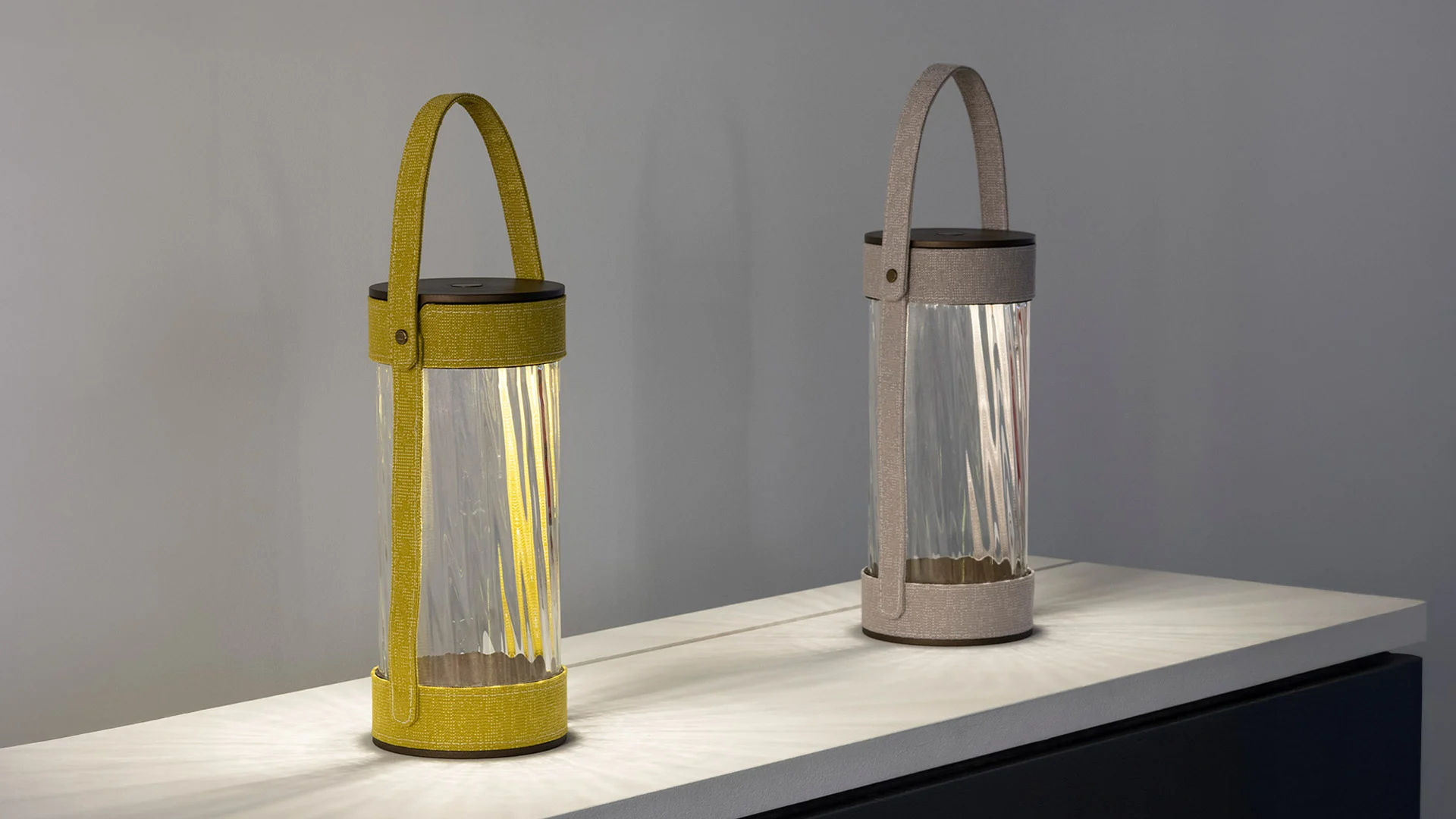 Two lanterns with ribbed glass cylinders and yellow and grey fabric straps on a lit shelf – AlUla Lantern for Artemide, Milan, Italy, 2025 – lighting design
