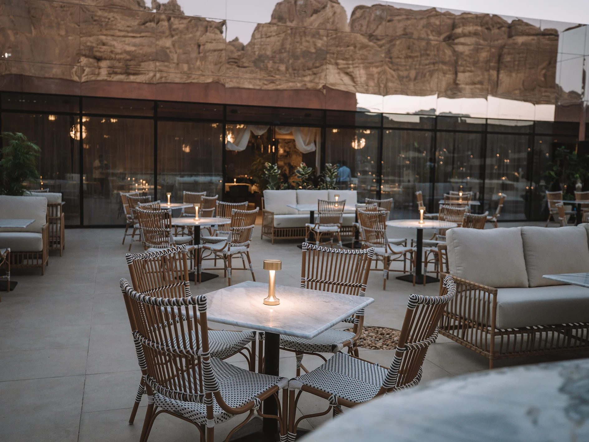 Rooftop restaurant terrace at dusk with lit tables, the mirror wall reflecting rocks and a cliff behind – Maraya Concert Hall, AlUla, Saudi Arabia, 2019 – architecture
