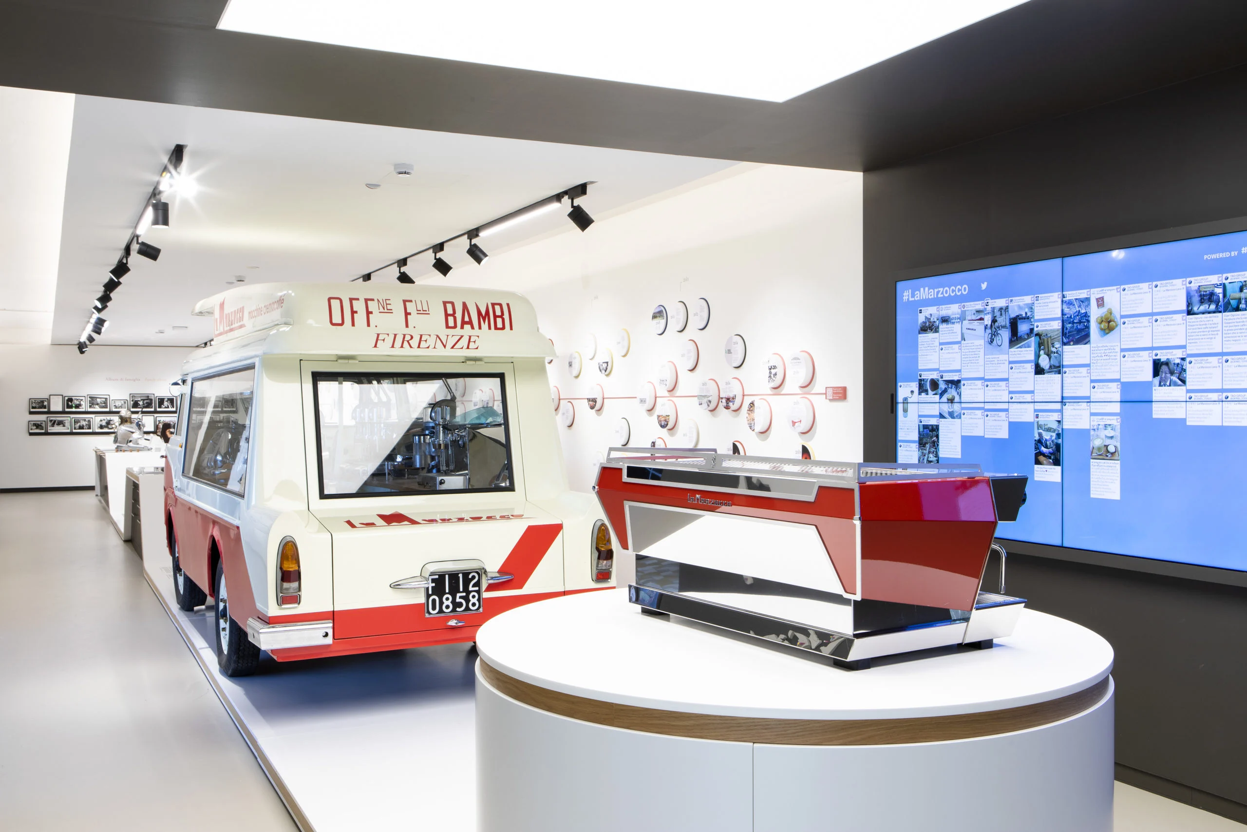 Red espresso machine on a round plinth beside a vintage van and a digital photo wall – La Marzocco Accademia del Caffè Espresso, Florence, Italy, 2018 – interior design