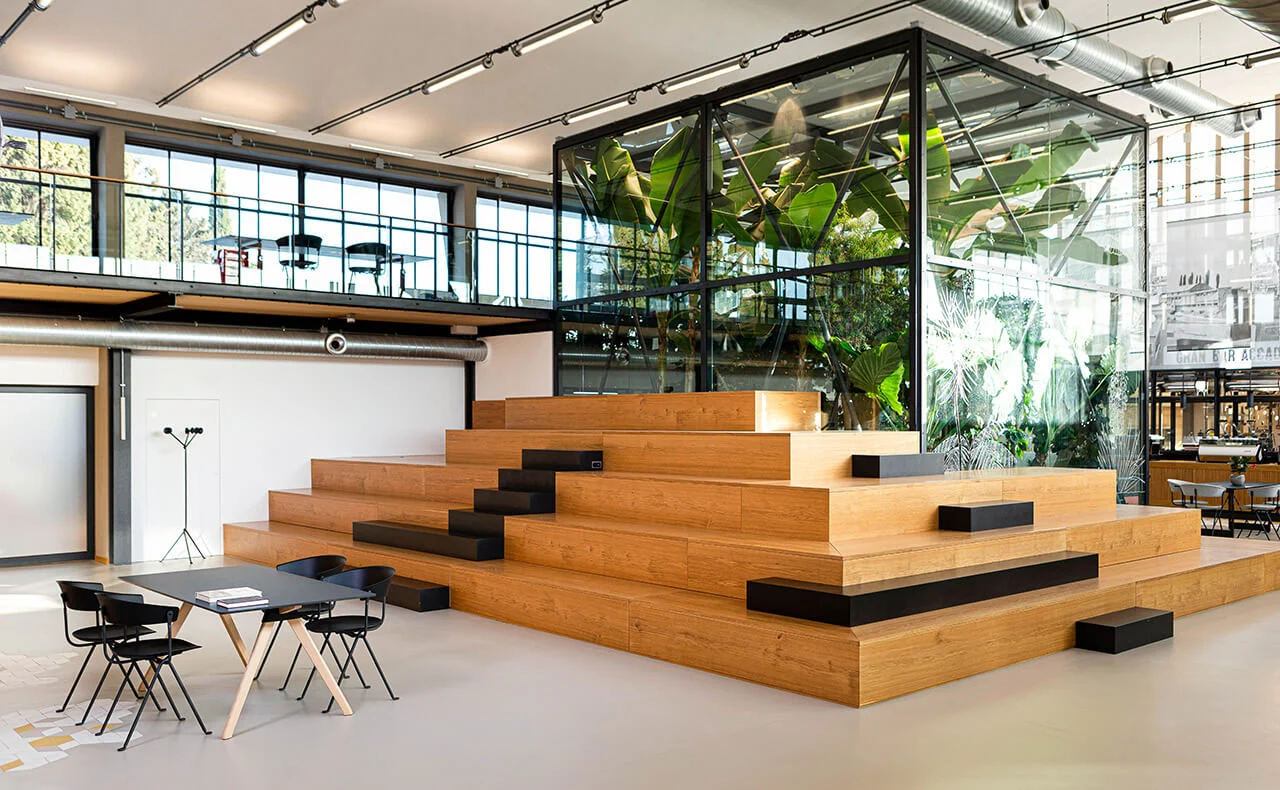 Large oak stepped seating with black cushions in front of the glass greenhouse and a mezzanine – La Marzocco Accademia del Caffè Espresso, Florence, Italy, 2018 – interior design