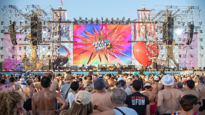 Daytime beach crowd before the Jova Beach Party stage: scaffold towers, a colourful logo screen and a giant red heart – Jova Beach Party 2022, Italy – concert stage design