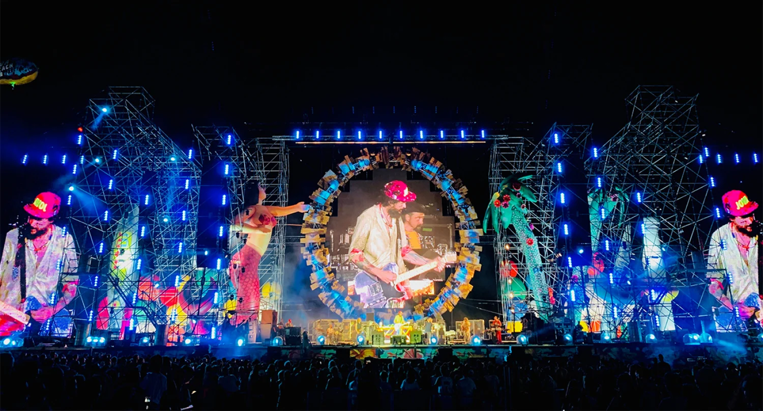 Night view of the Jova Beach stage: blue-lit scaffolding towers and screens showing the singer inside a colourful ring – Jova Beach Party 2022, Italy – concert stage design