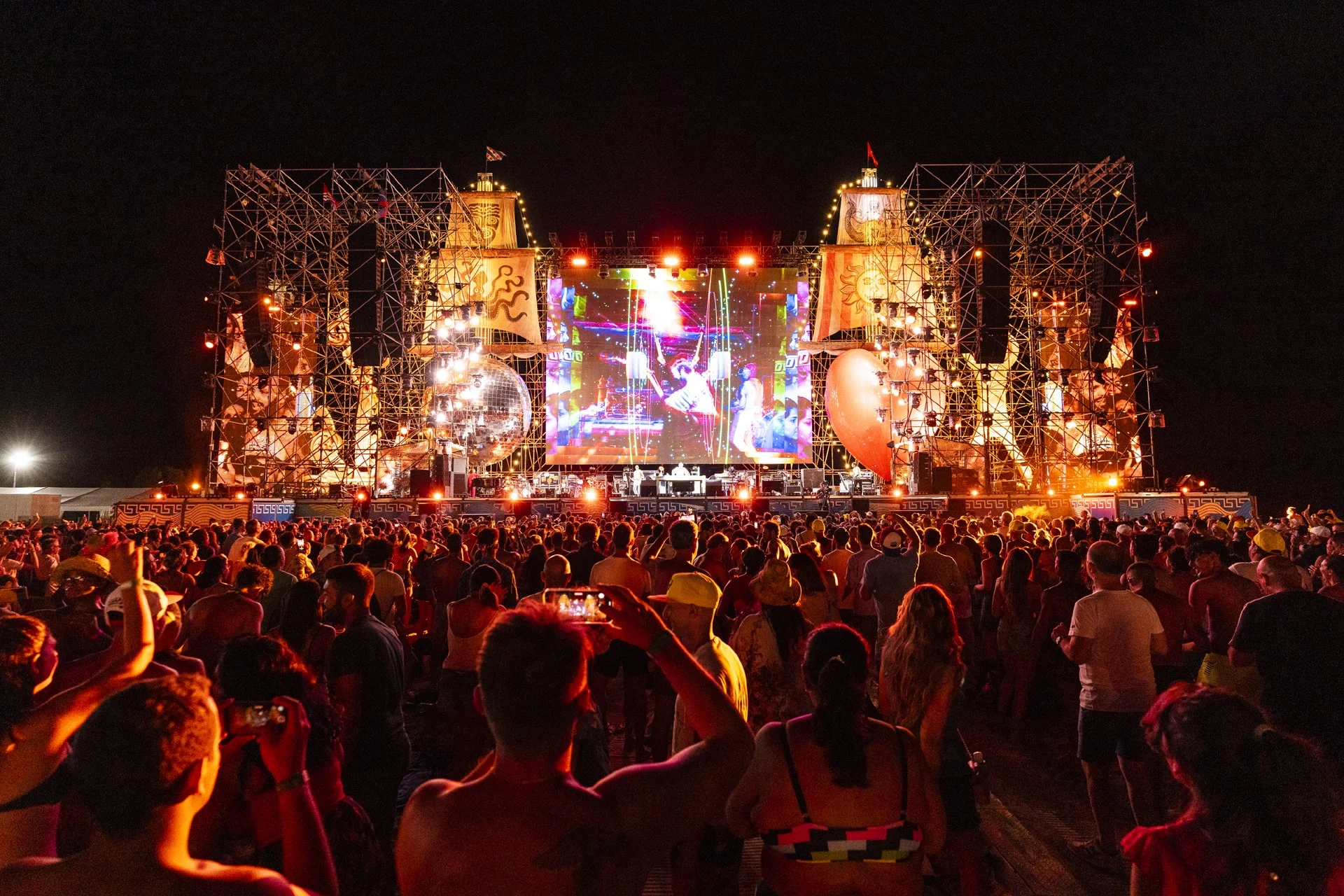 Night view from the crowd, phones raised towards the lit scaffold stage with ship-like towers and a central screen – Jova Beach Party 2022, Italy – concert stage design