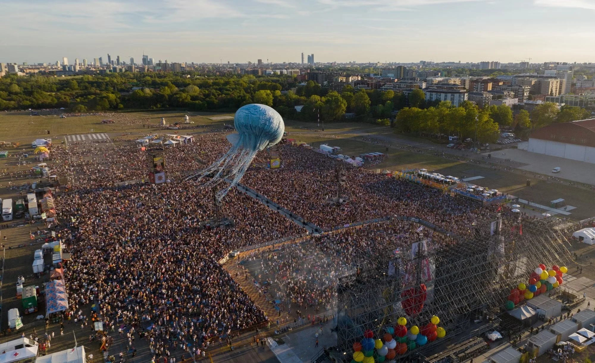 Aerial view of the concert crowd in a park, the jellyfish aerostat floating above and the city skyline beyond – Jova Beach Party 2022, Italy – concert stage design