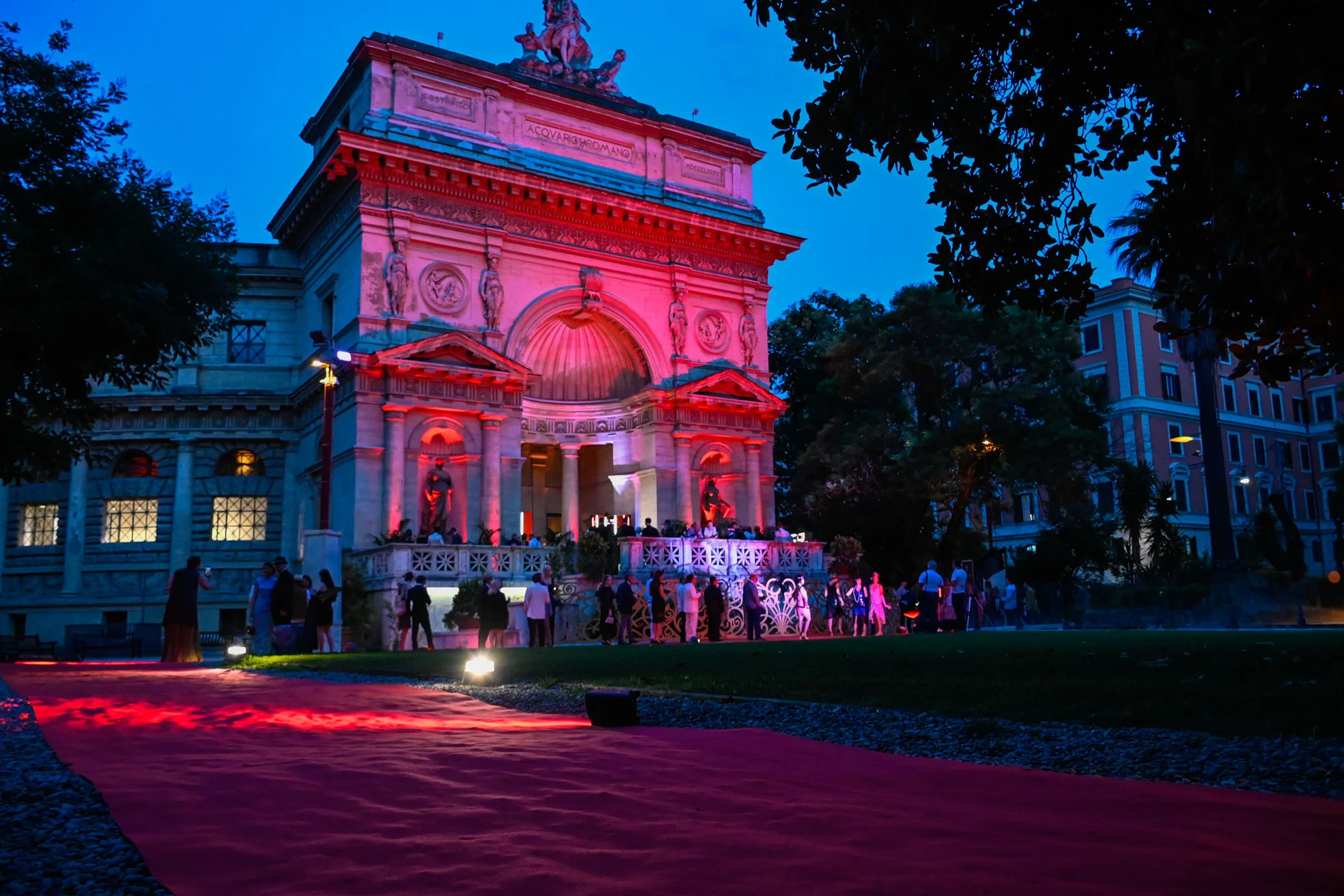 Historic arched building lit pink at dusk, guests gathered at the end of a long red carpet – Campari Cavalcade, Rome, Italy, 2023 – event design