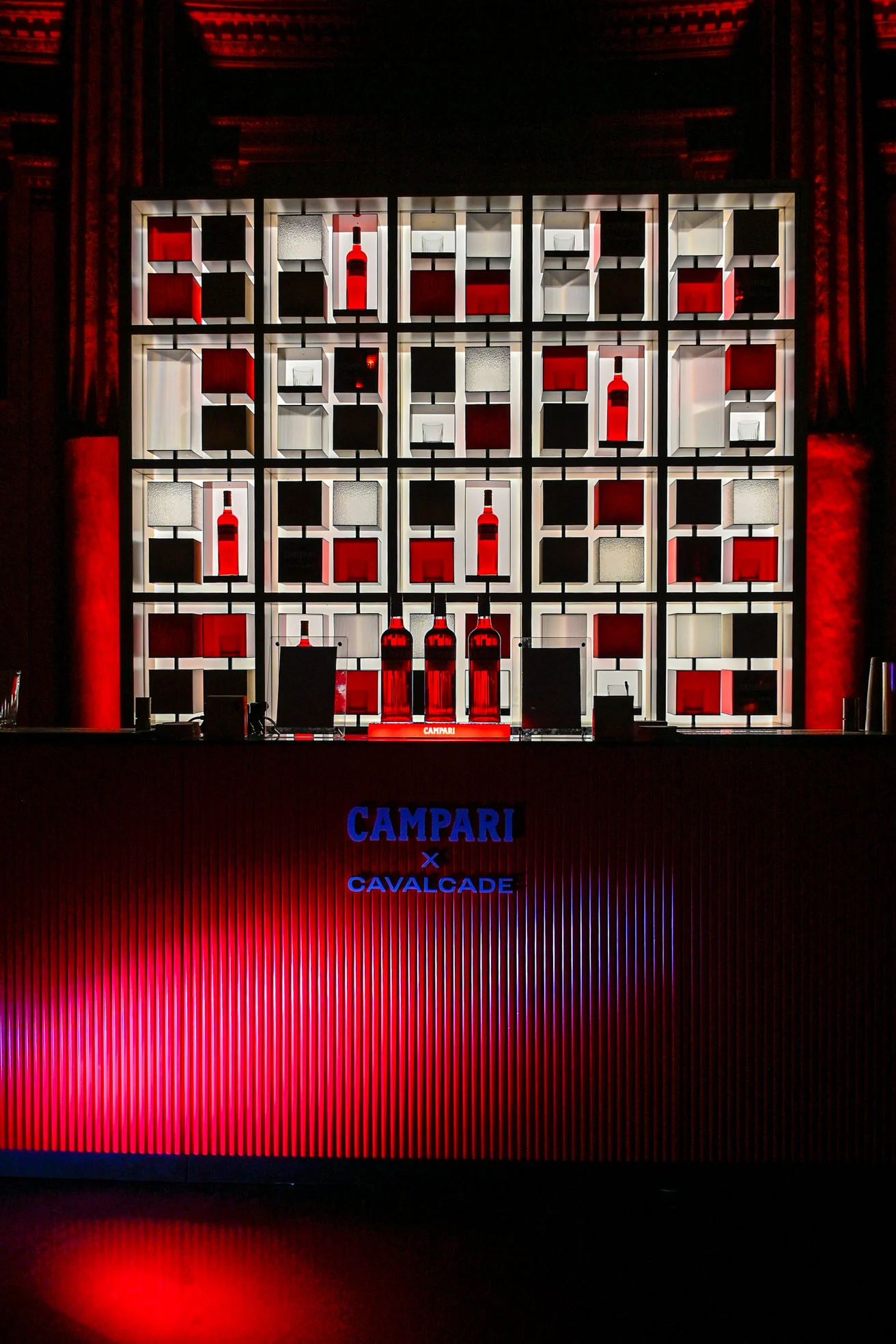 Backlit grid shelving with Campari bottles behind a red-lit Campari x Cavalcade bar counter – Campari Cavalcade, Rome, Italy, 2023 – event design