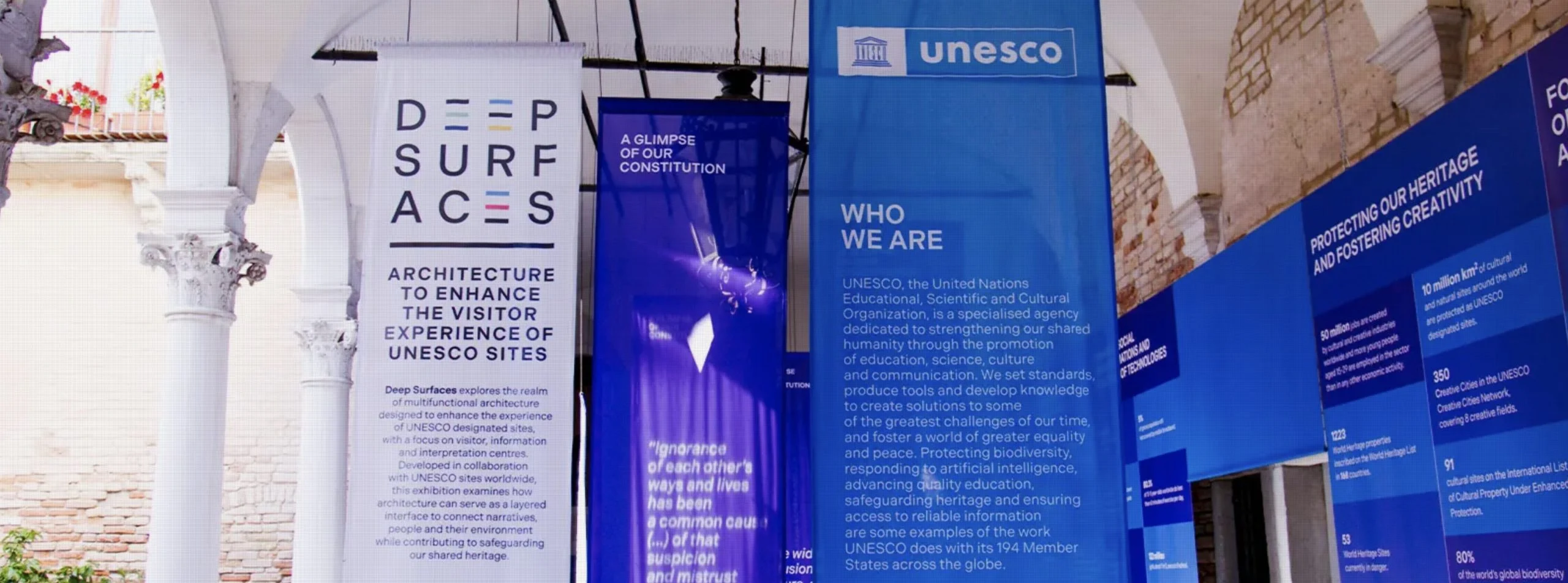 Hanging Deep Surfaces and UNESCO banners in blue and white between the columns of the Palazzo Zorzi courtyard – Deep Surfaces at Palazzo Zorzi, Venice, Italy, 2025 – exhibition design
