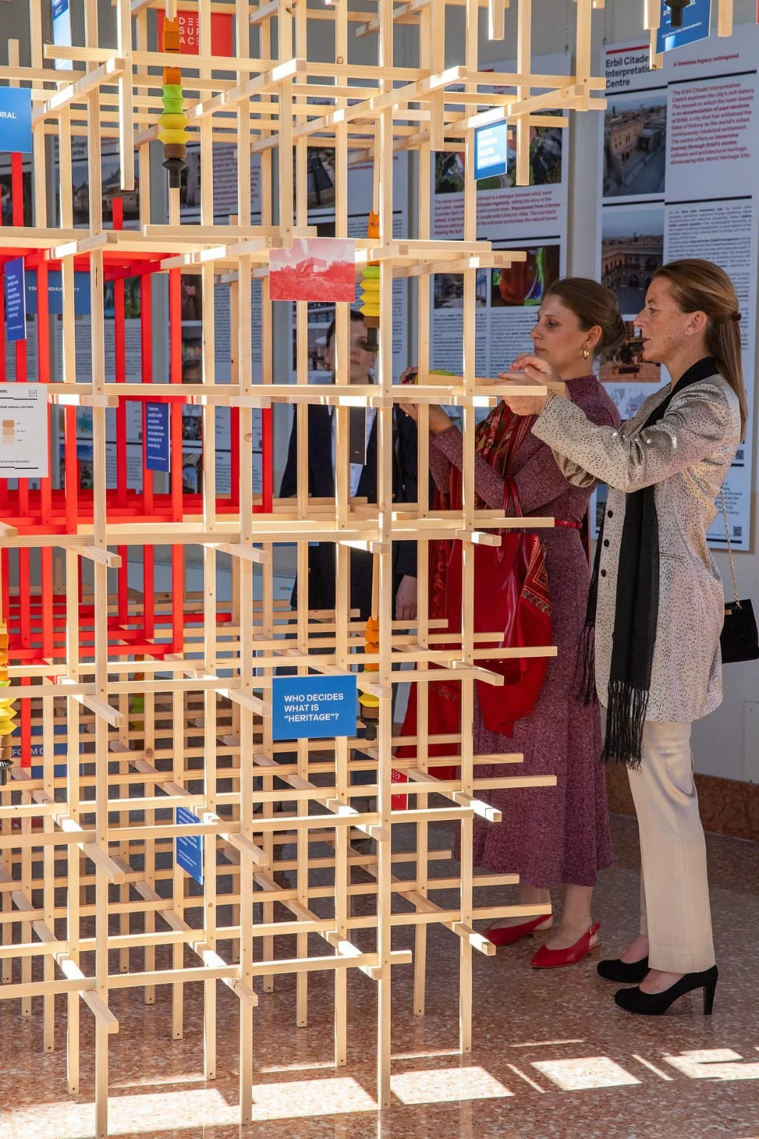 Visitors placing a piece inside the tall wooden lattice installation, sunlight on the marble floor – Deep Surfaces at Palazzo Zorzi, Venice, Italy, 2025 – exhibition design