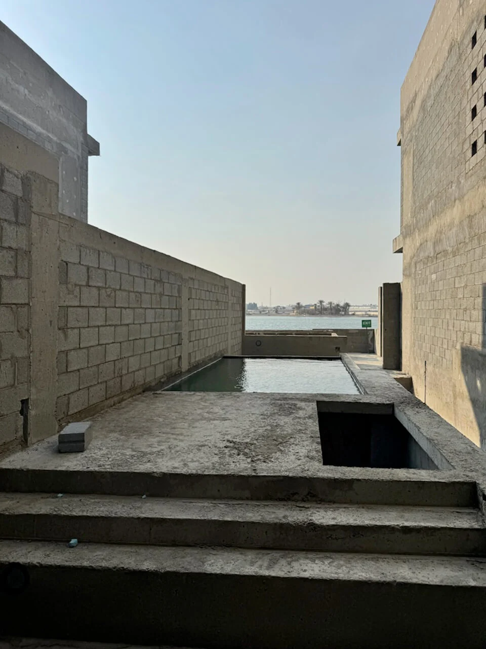 Concrete steps leading to an unfinished pool between block walls, with the sea beyond – Radic Residences, Jeddah, Saudi Arabia, 2025 – architecture, under construction