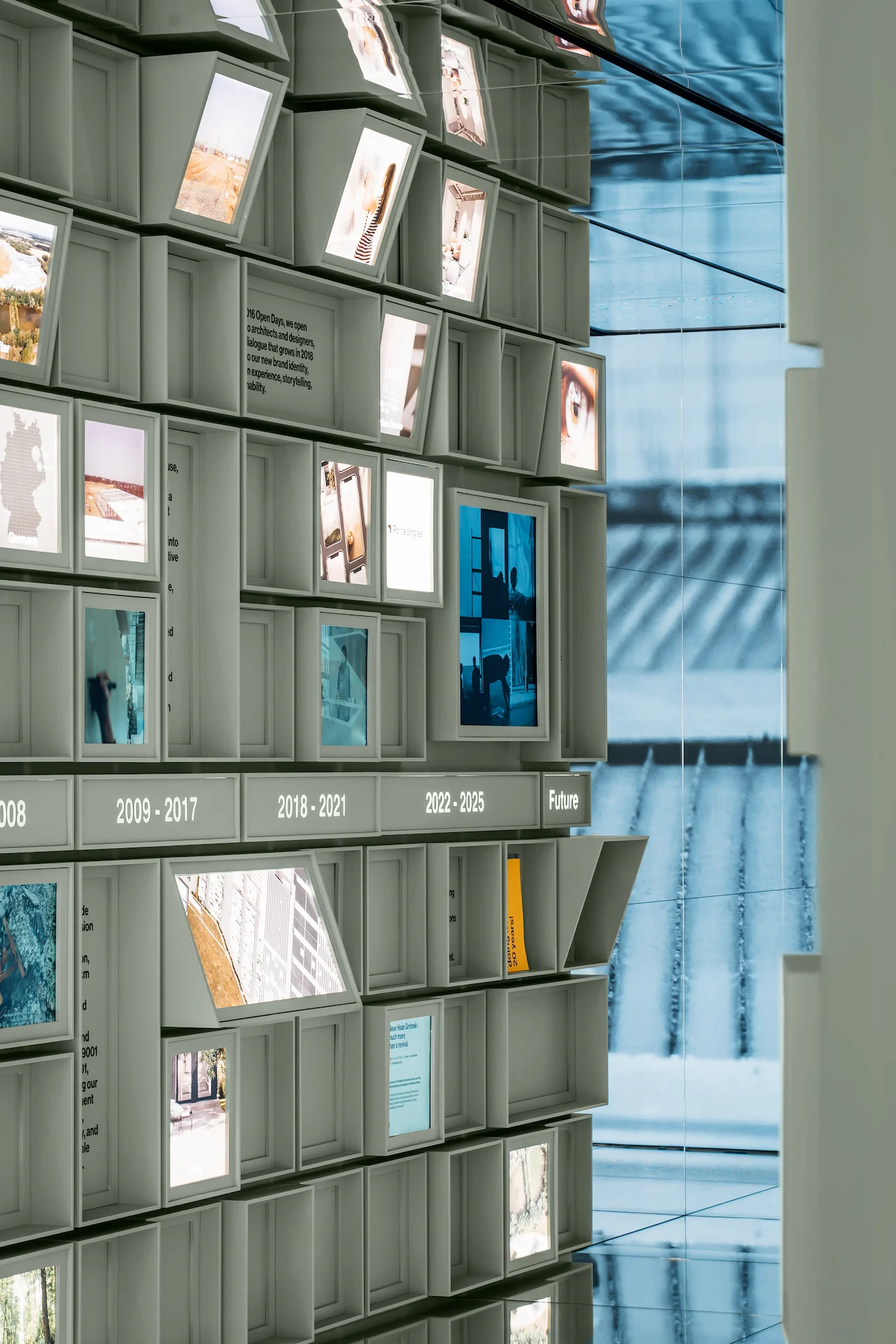 Detail of the sage-green cube grid with tilted screens, images and the timeline years up to Future – Porcelaingres Brand Narrative Space, Castellarano, Italy, 2025 – showroom design