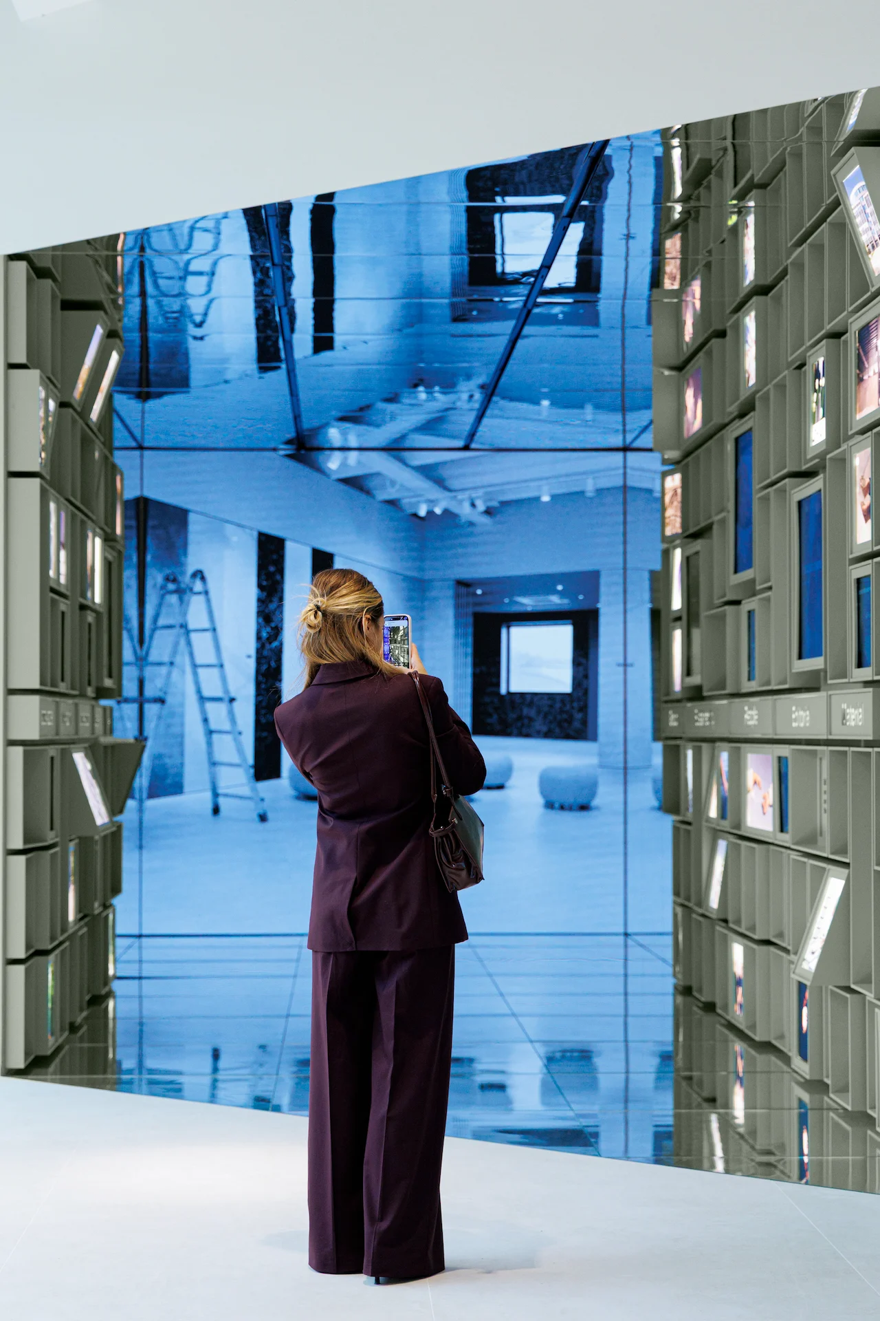Visitor photographing a large video wall at the end of the mirrored passage – Porcelaingres Brand Narrative Space, Castellarano, Italy, 2025 – showroom design