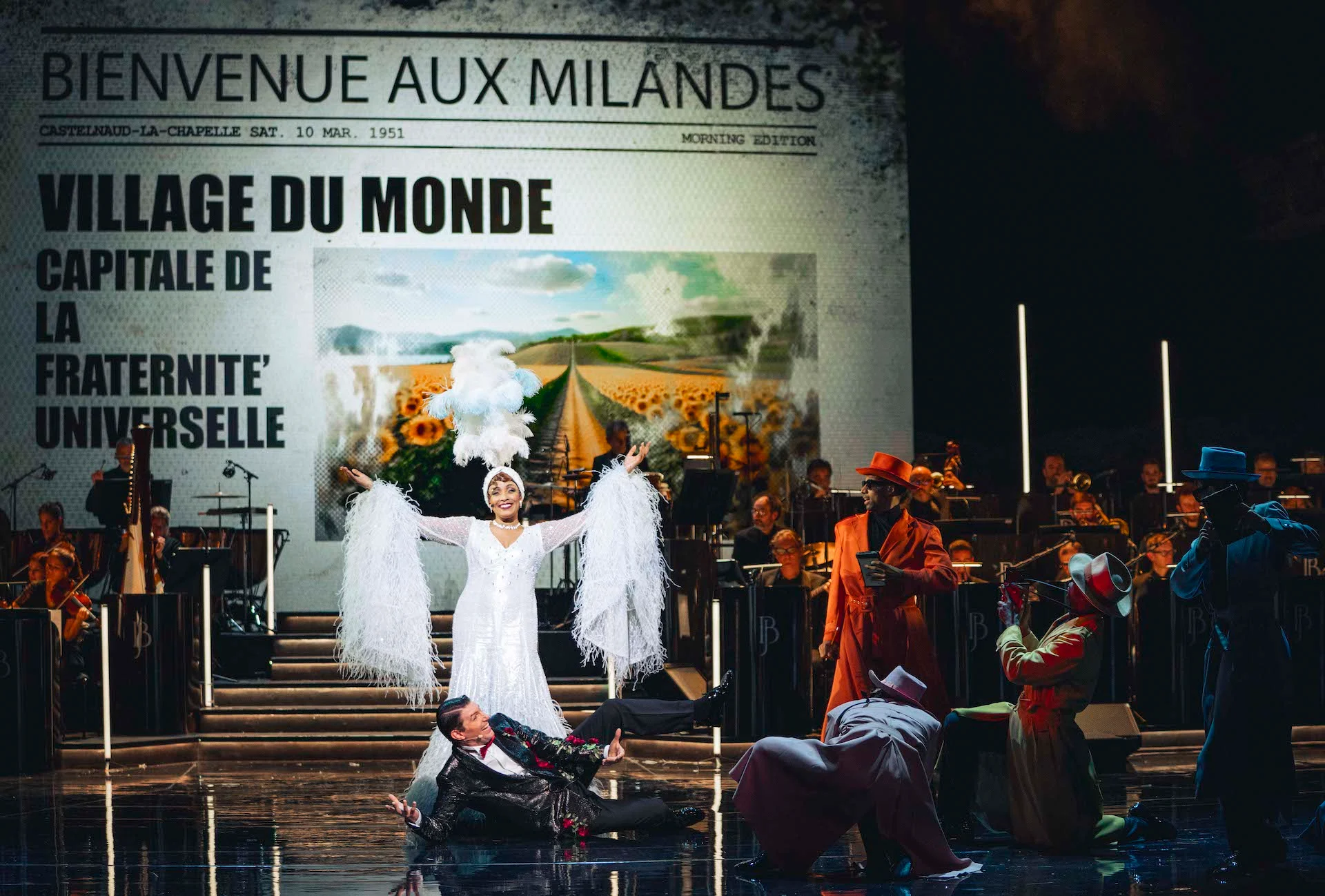 Singer in a white feathered costume before a giant newspaper page reading Bienvenue aux Milandes – Bonsoir Monte-Carlo, Monte Carlo, Monaco, 2025 – stage design