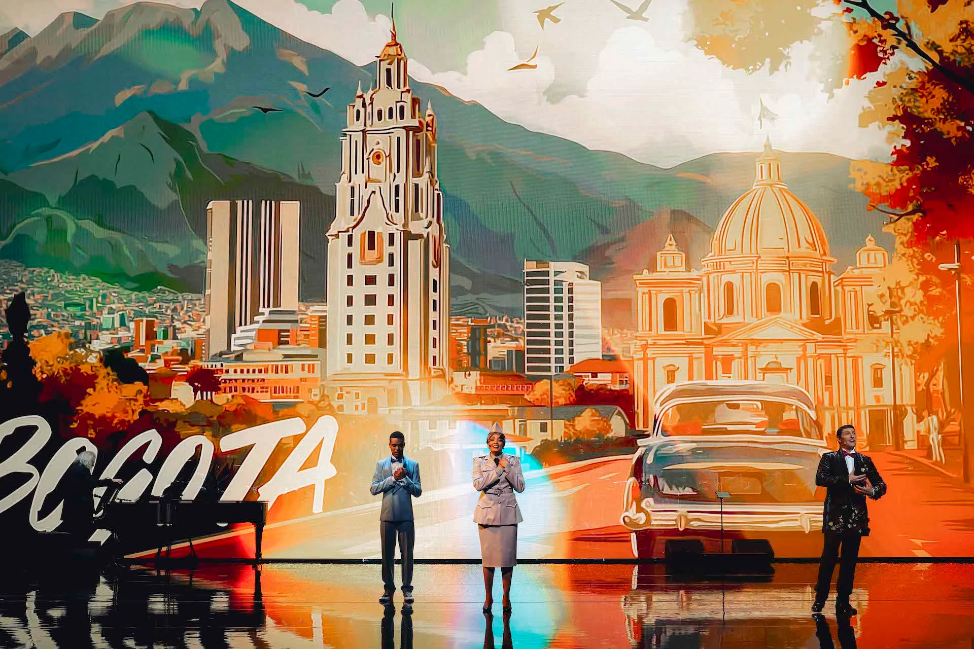 Three singers before an illustrated backdrop of Bogotá with mountains, towers, a domed church and a vintage car – Bonsoir Monte-Carlo, Monte Carlo, Monaco, 2025 – stage design