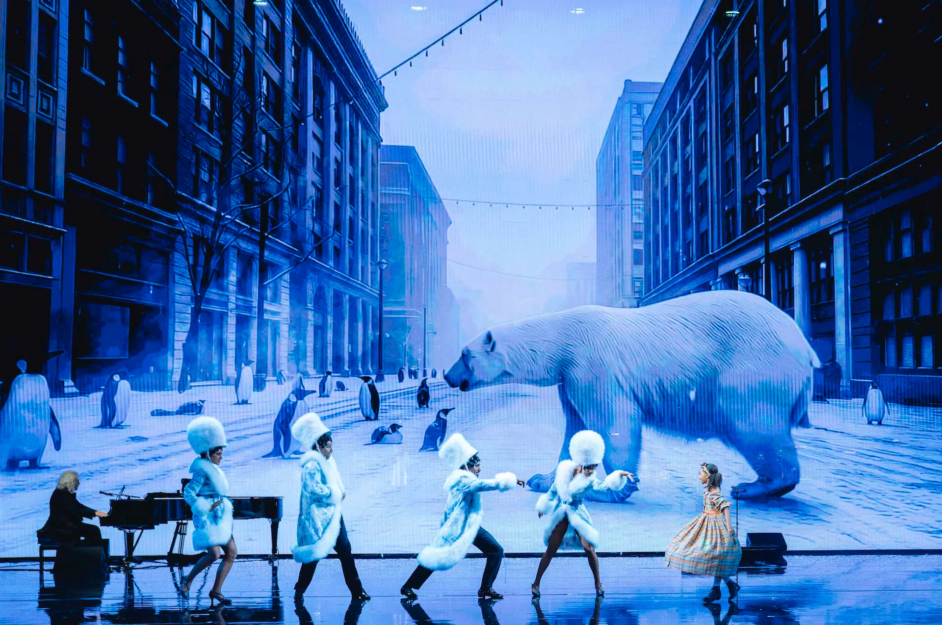 Dancers in white fur costumes before a projected snowy city street with a polar bear and penguins – Bonsoir Monte-Carlo, Monte Carlo, Monaco, 2025 – stage design